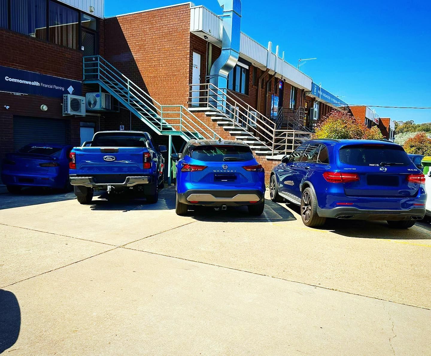 Four blue vehicles parked in front of a brick building with stairs; sunny day. —	Diamond Tints In Phillip, ACT