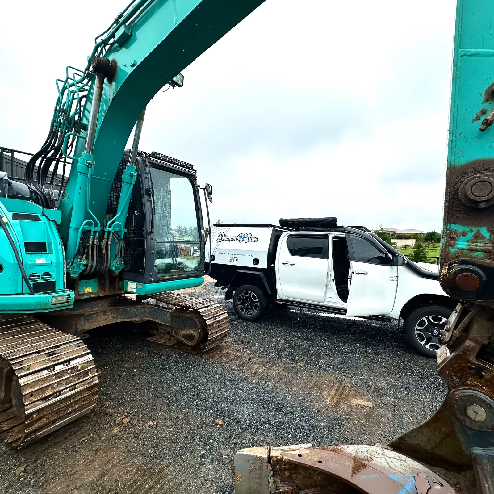 A Blue tractor is parked next to a white ute on the gravel — Diamond Tints In Belconnen, ACT