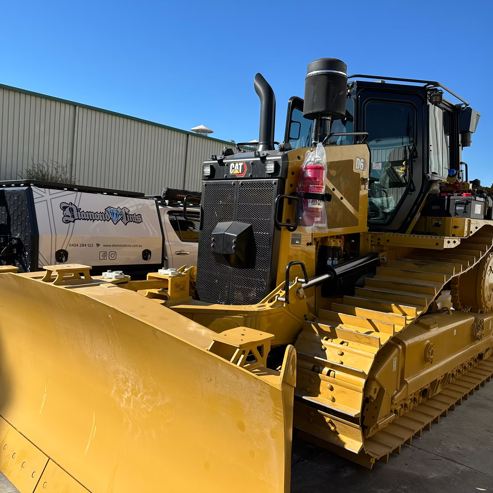 A yellow bulldozer with tinted windows is parked next to a ute — Diamond Tints In Phillip, ACT