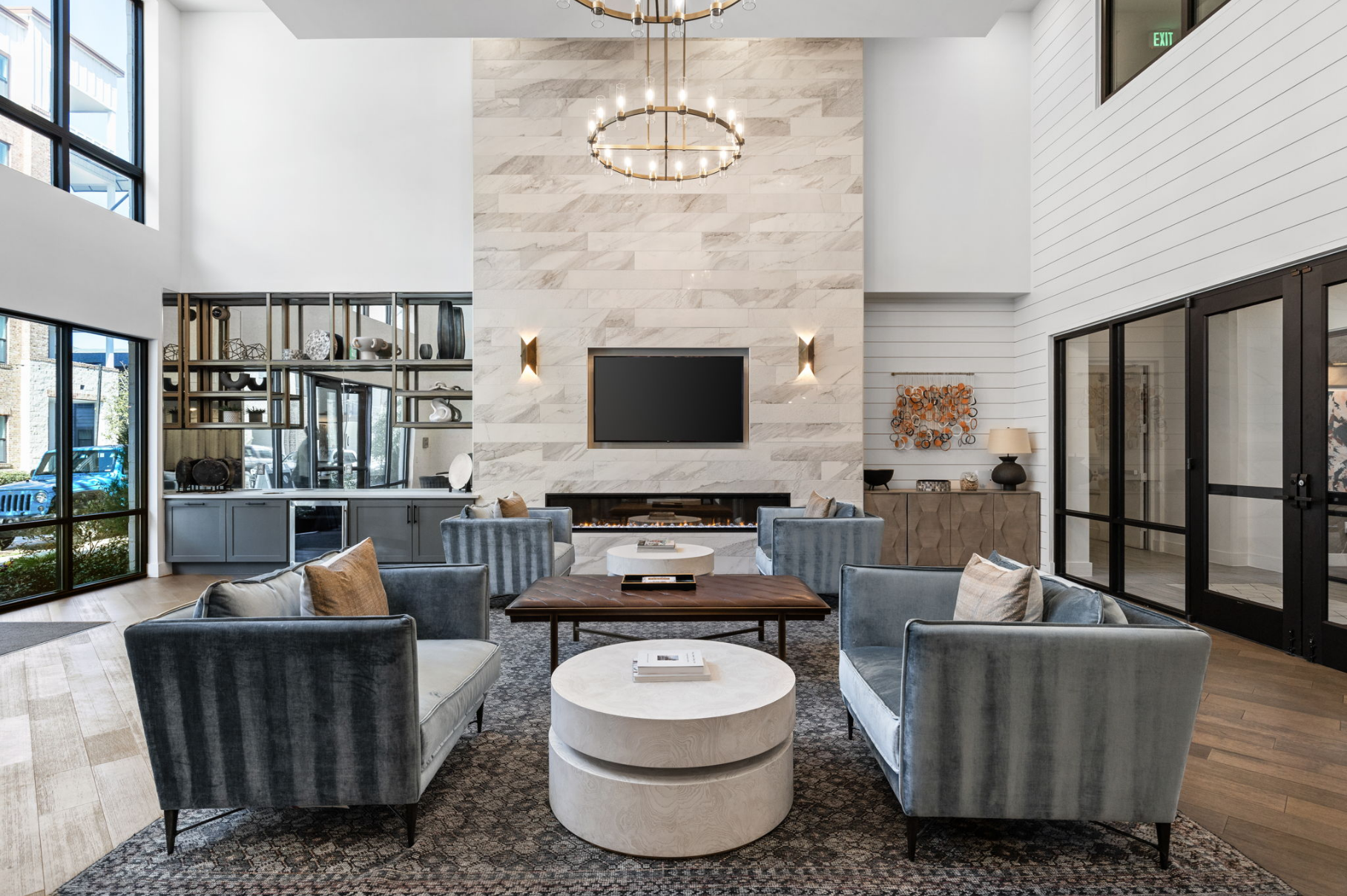 Lounge area with blue velvet seating, fireplace, large windows, and a circular chandelier.