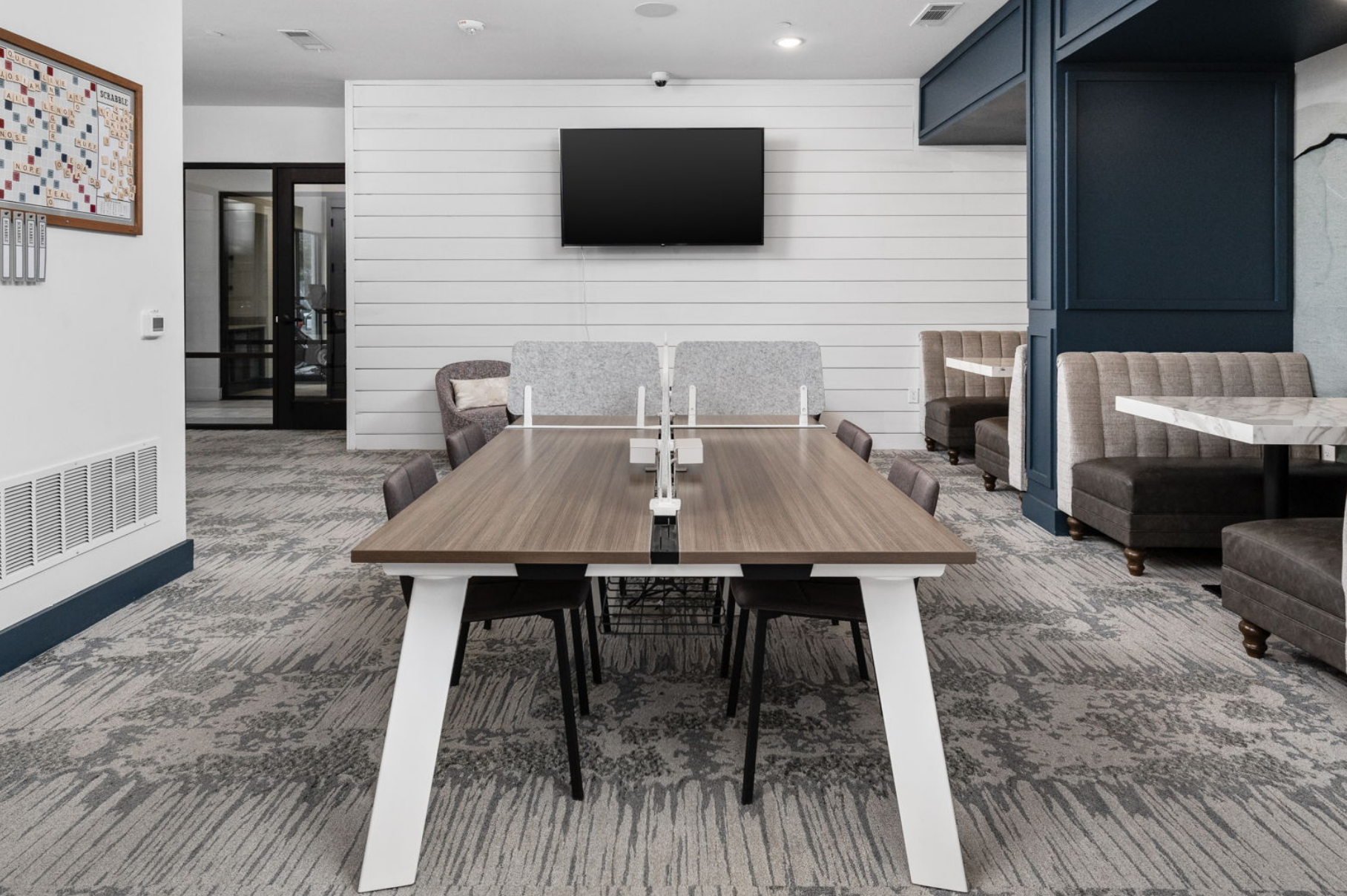 Modern co-working space with long wooden table, TV, and lounge seating.