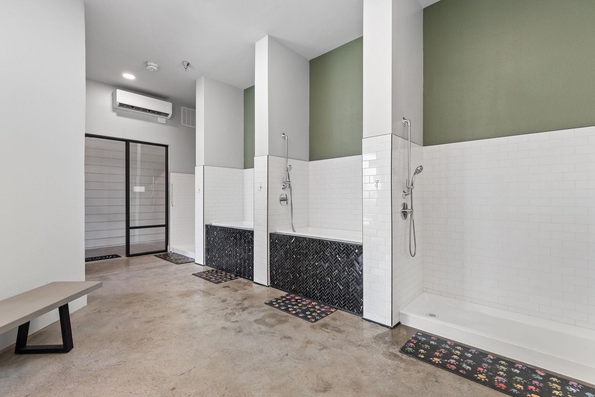 A room with a bench and three dog-washing stations featuring black tiled bases, wall-mounted sprayers, and green walls.