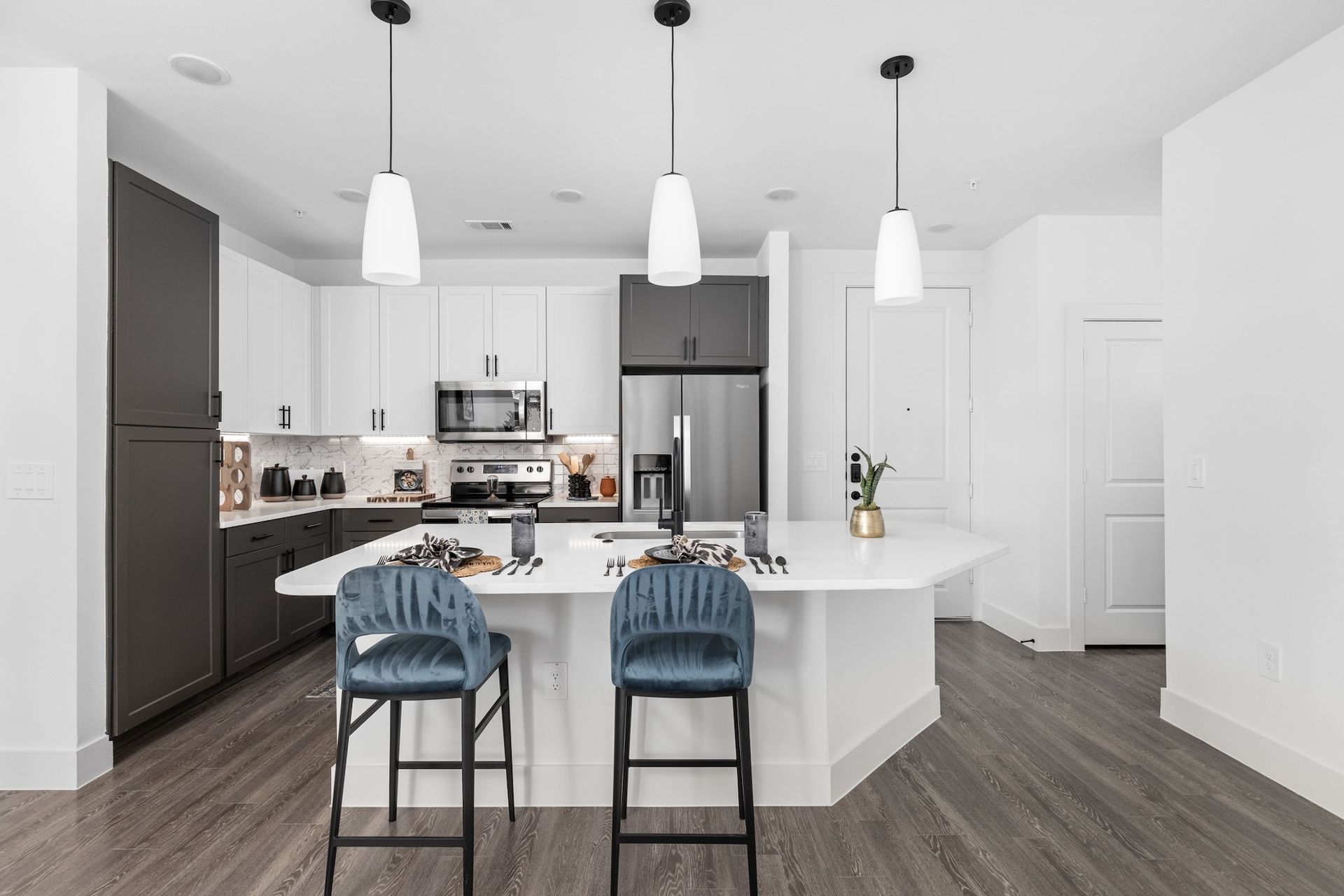 Modern kitchen with white island, gray and white cabinets, stainless steel appliances, and blue bar stools.