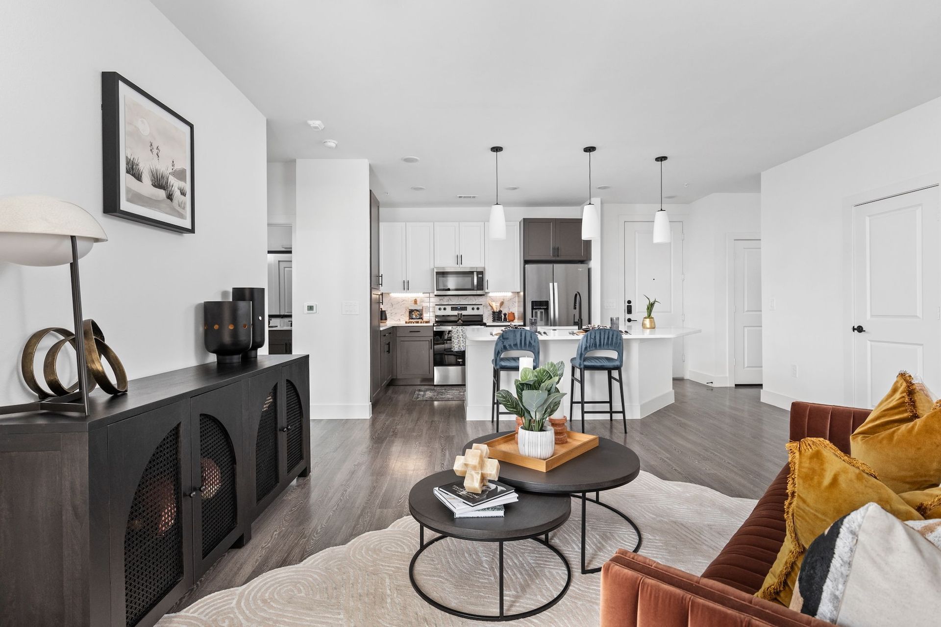 Modern living room with open kitchen, dark wood console, brown sofa, and small coffee tables.