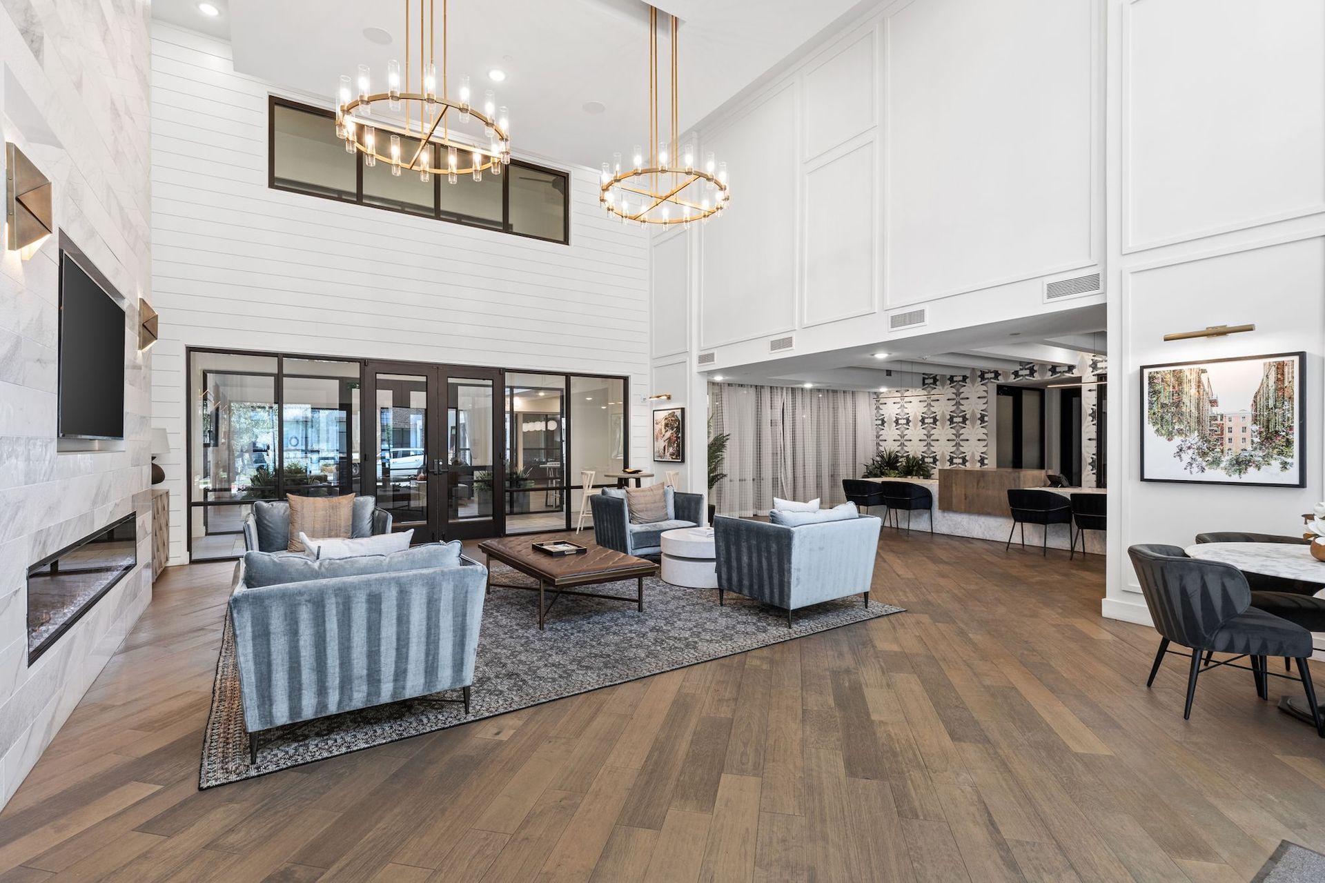 A spacious lobby with high ceilings, blue armchairs on a patterned rug, a fireplace, and warm wood flooring.