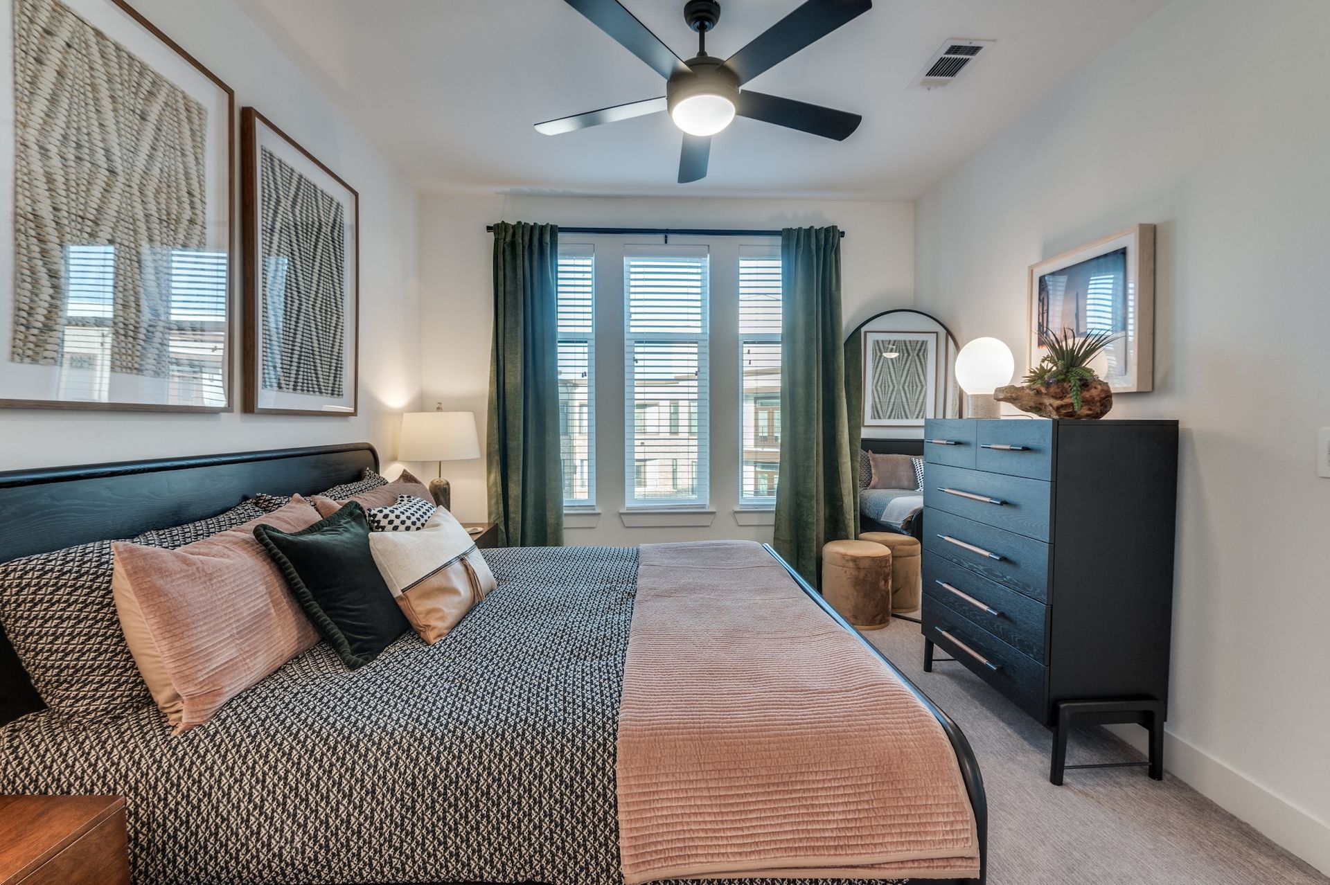 Bedroom with a bed, black dresser, large window with green curtains, and art.