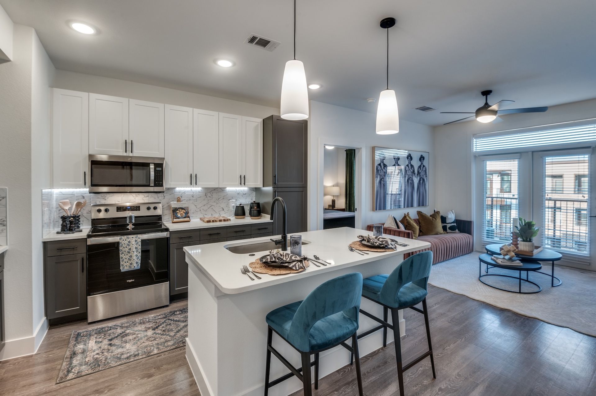 Modern apartment with white kitchen cabinets, a central island with teal barstools, and an adjoining living area.