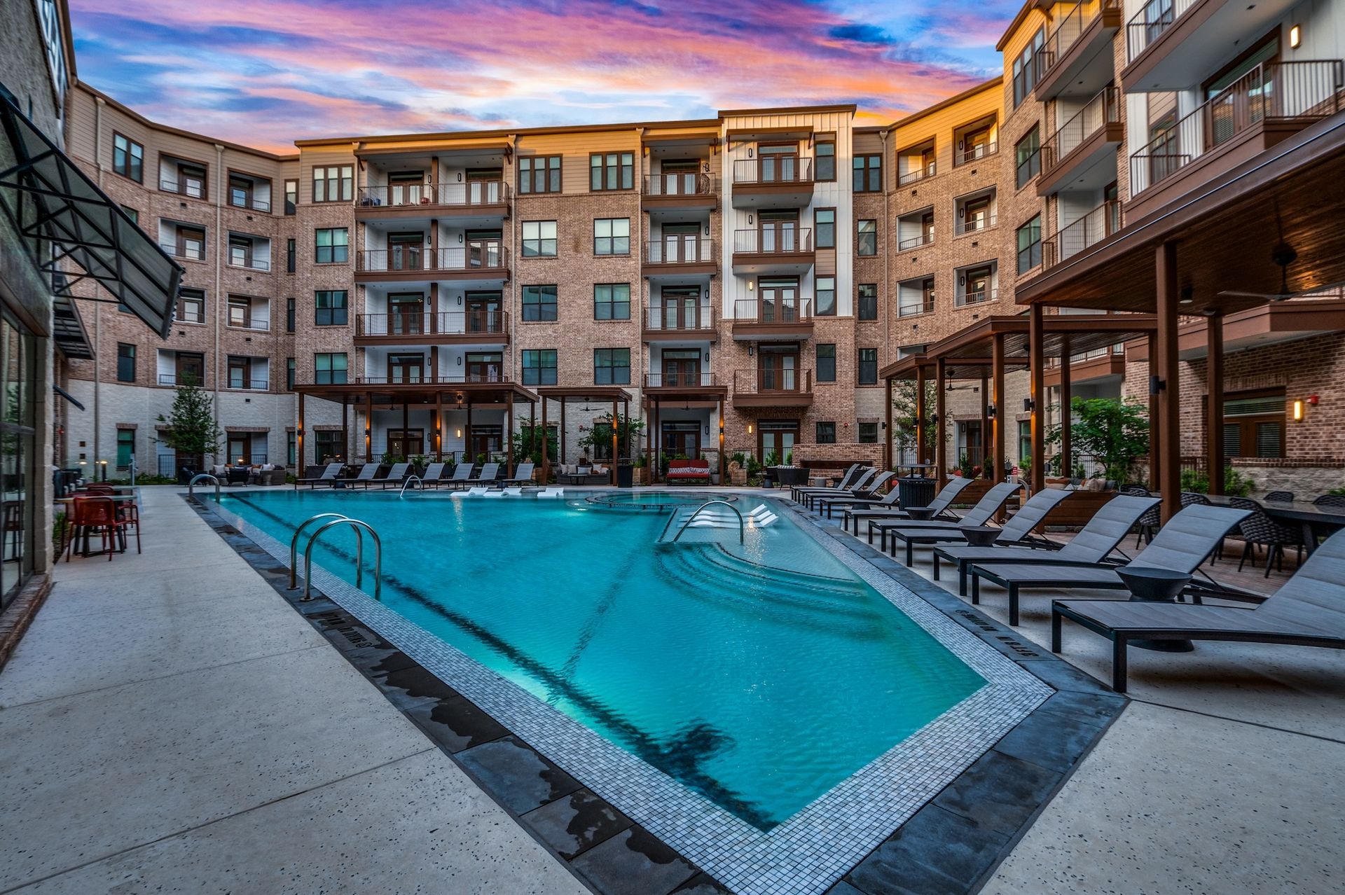 An outdoor pool in an apartment complex courtyard; lounge chairs surround the turquoise water.
