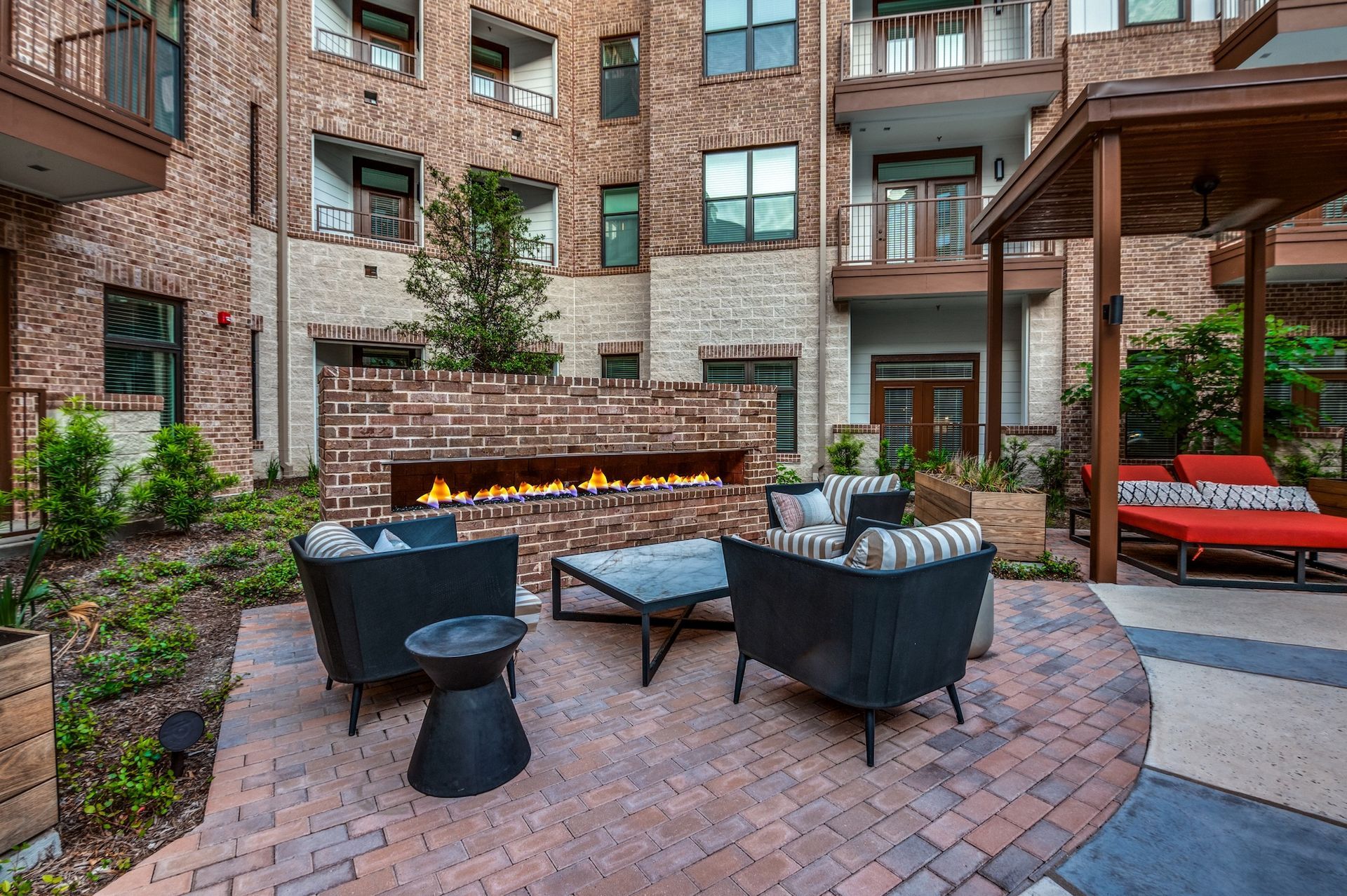 Brick patio with seating, fireplace, and lounge area, surrounded by a brick building.