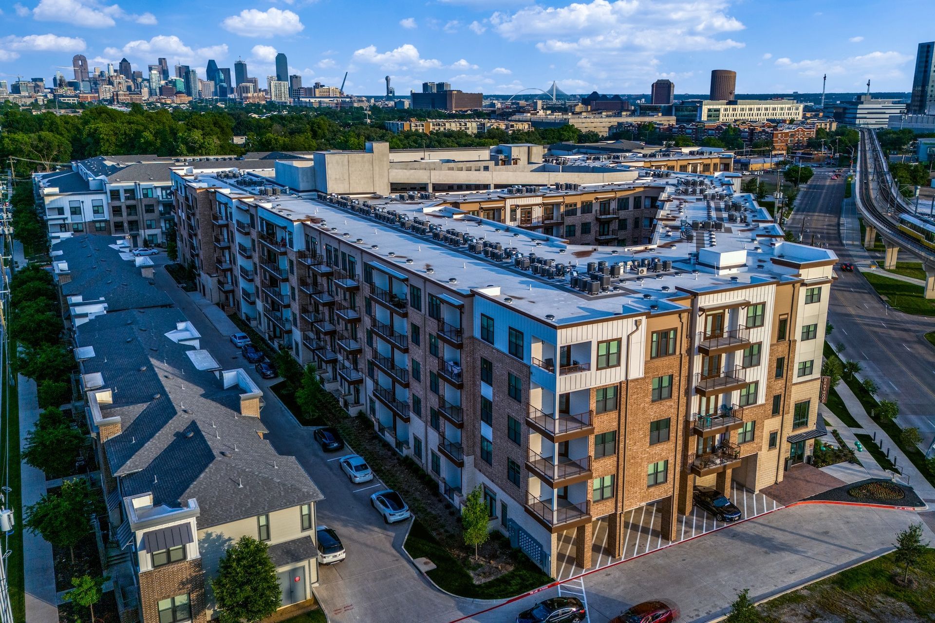 Aerial view of a multi-story apartment complex near a city skyline under a clear blue sky.