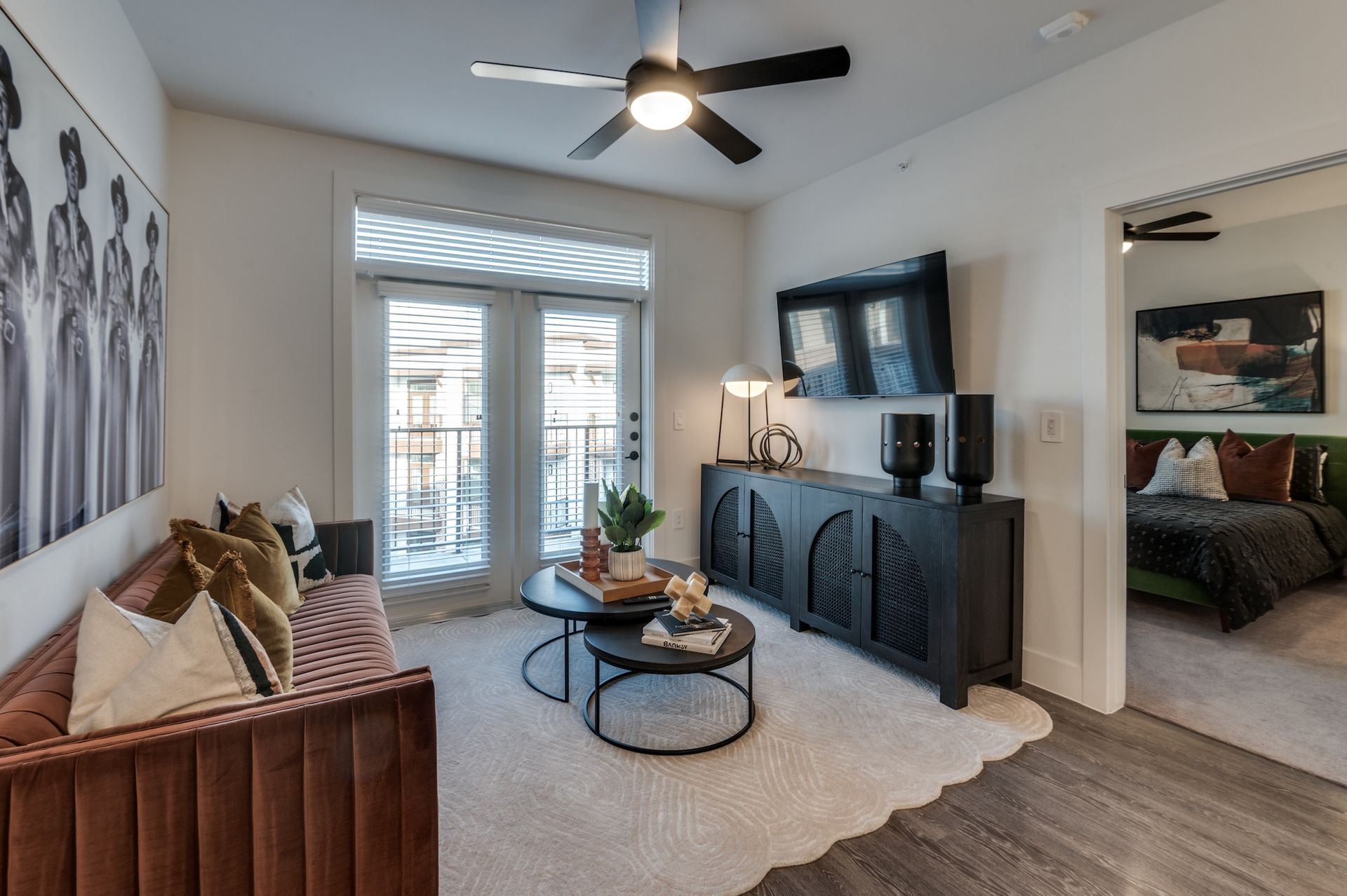 A living room with a velvet sofa, two round coffee tables, a black cabinet, and a view of a balcony through glass doors.
