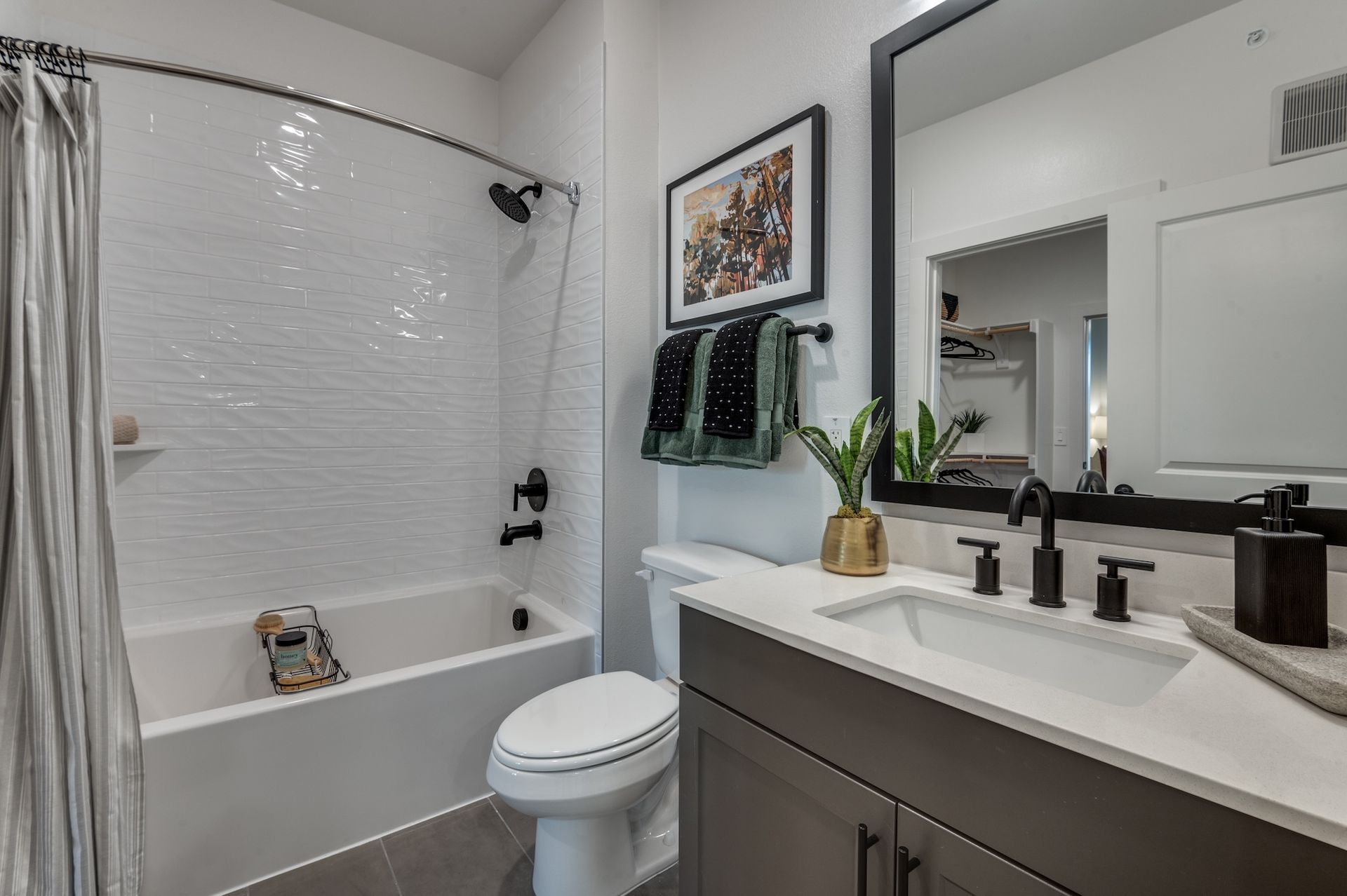 A modern bathroom with a white bathtub, toilet, grey vanity with a rectangular sink, and a black-framed mirror.