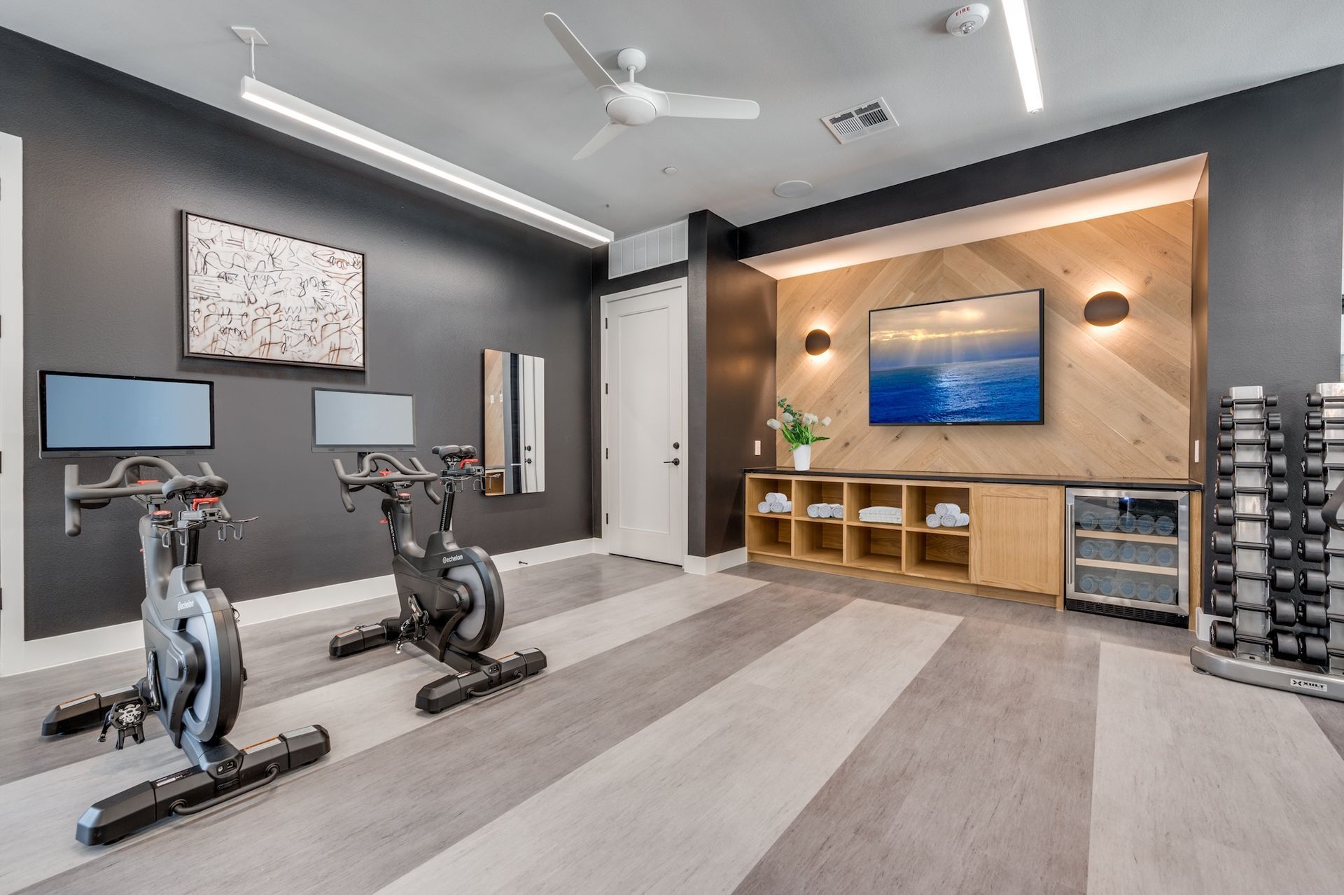 Indoor gym with exercise bikes, weights, TV, and decorative wood paneling.