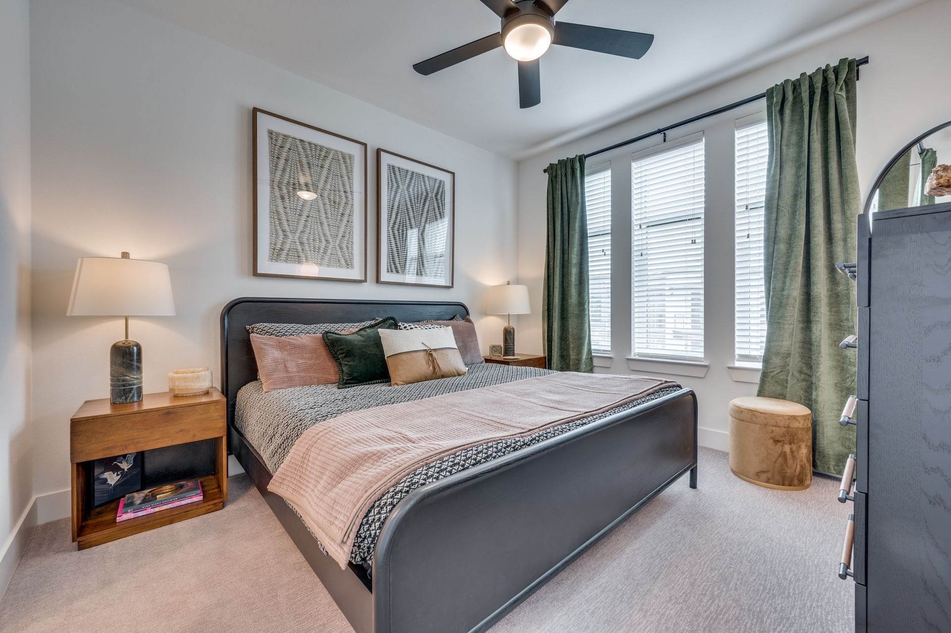 Bedroom with bed, nightstands, window with green curtains, framed art, and a small stool.