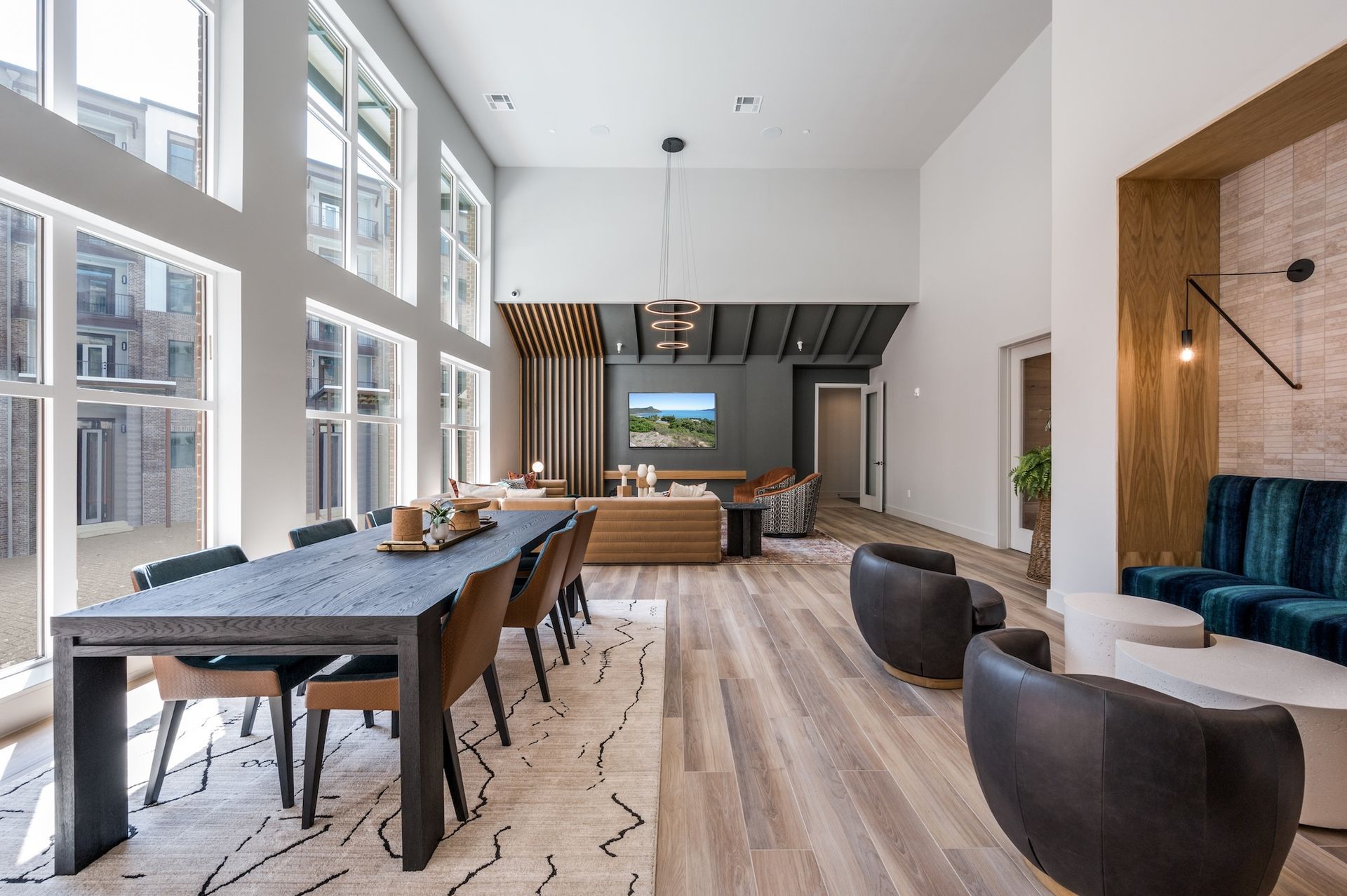 Modern lounge with large windows, dining table, seating areas, and a TV.