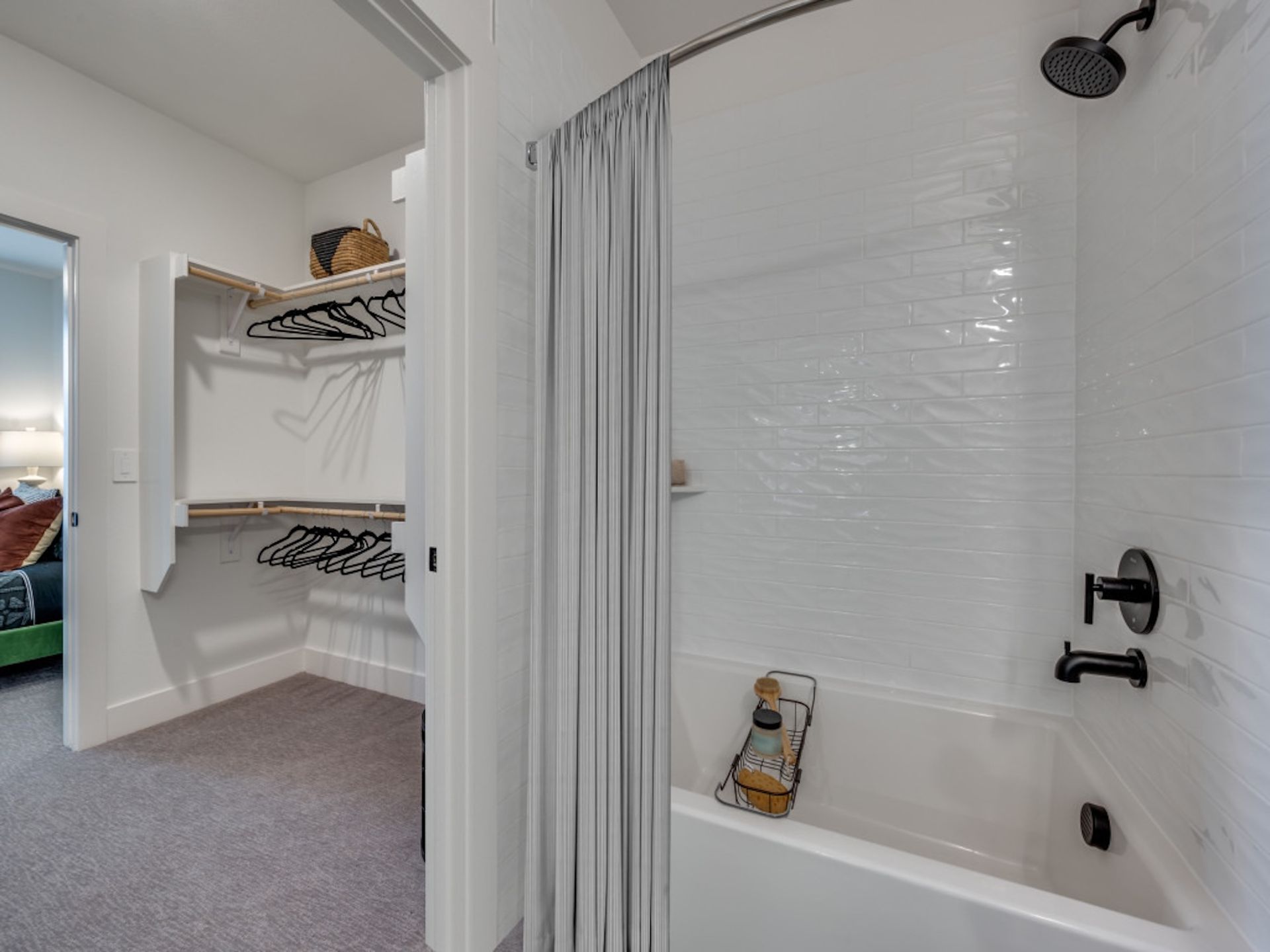 A white bathroom with a shower-tub combo and black fixtures, opening into a walk-in closet with carpeted flooring.