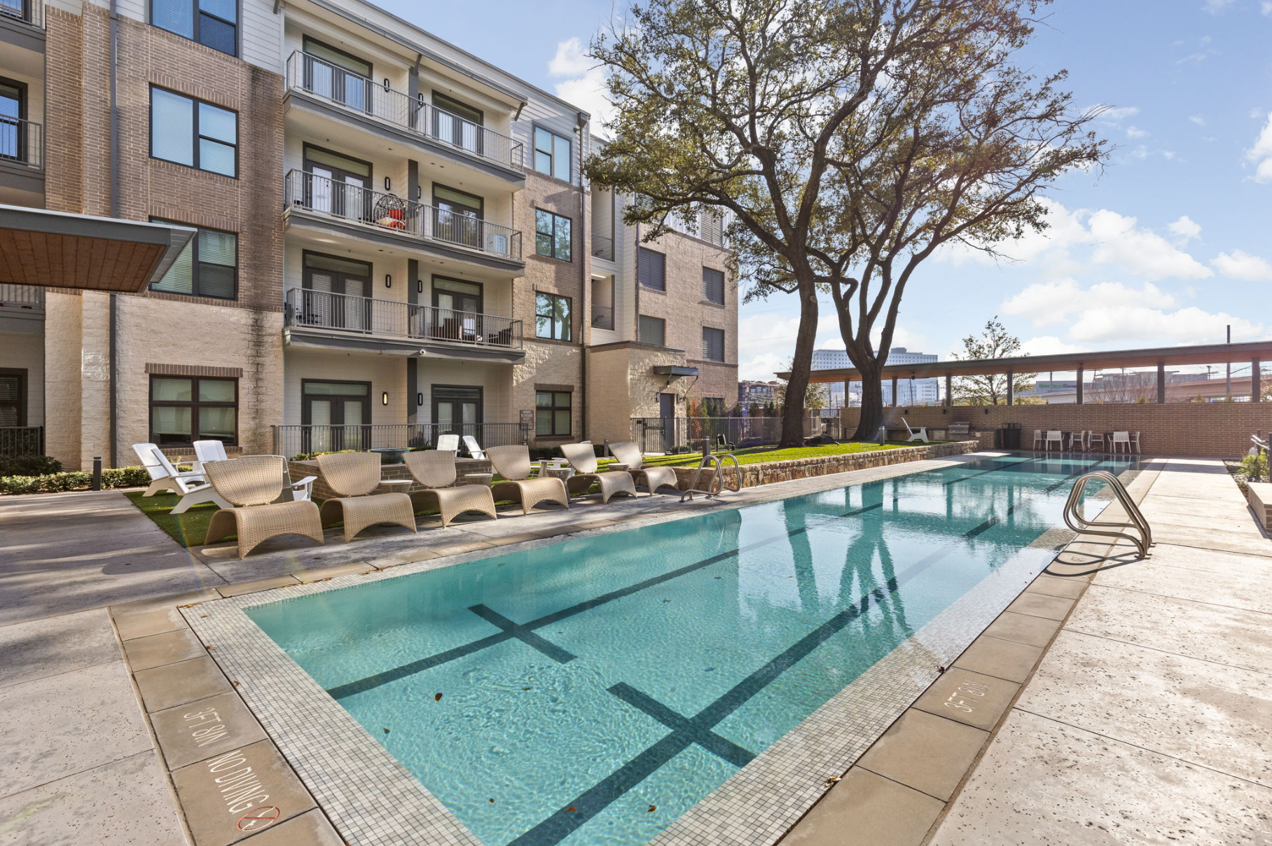 Swimming pool in front of an apartment building with lounge chairs. Sunny day, blue water.