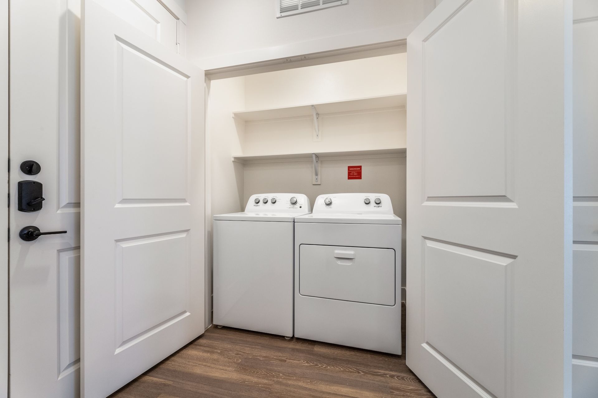 White washer and dryer in a laundry closet with open white doors and a shelf above.