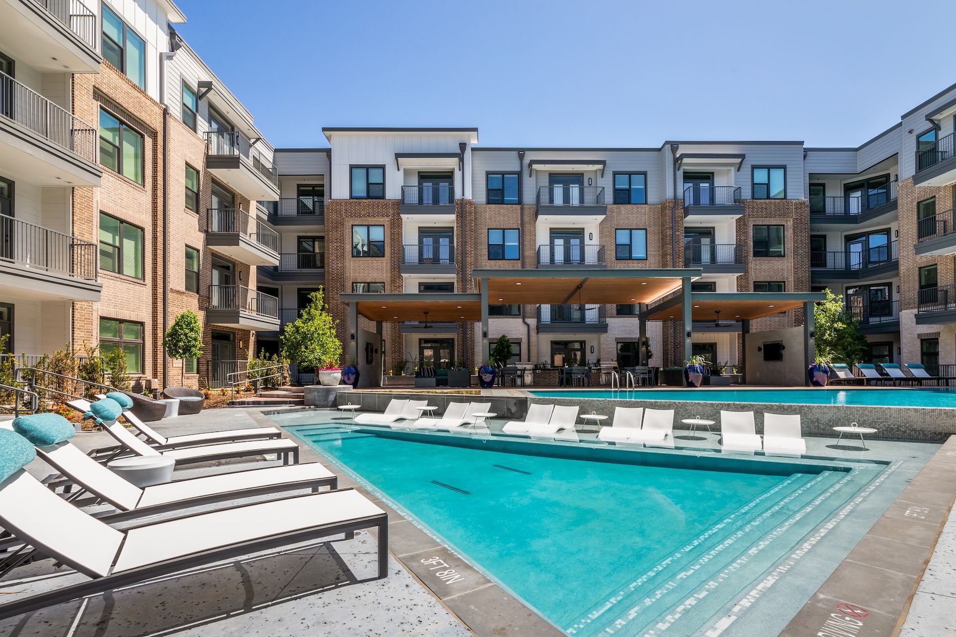 Pool area of a modern apartment complex with lounge chairs, blue water, and outdoor seating.