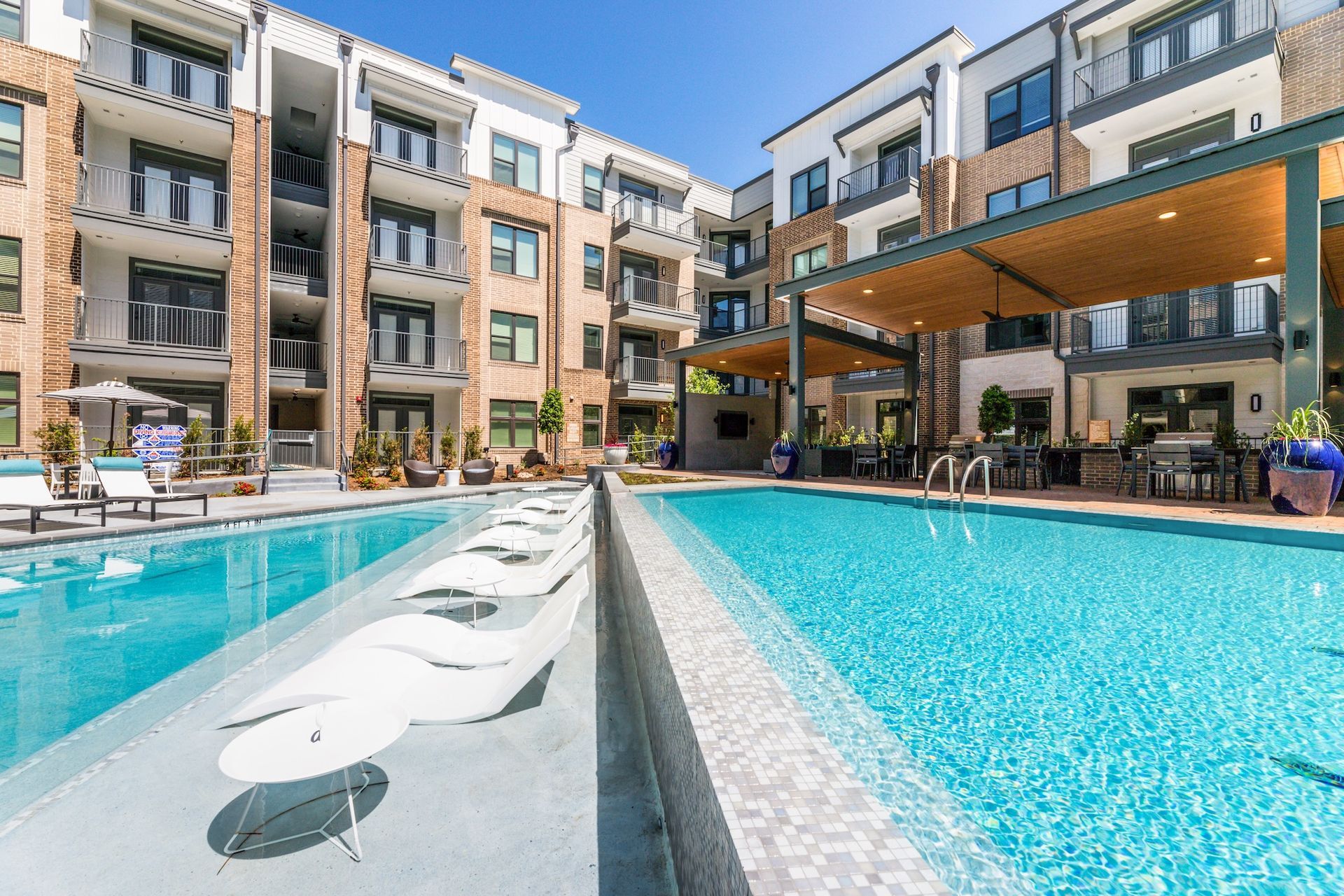 Pool with white lounge chairs, surrounded by apartment buildings and an open-air seating area.