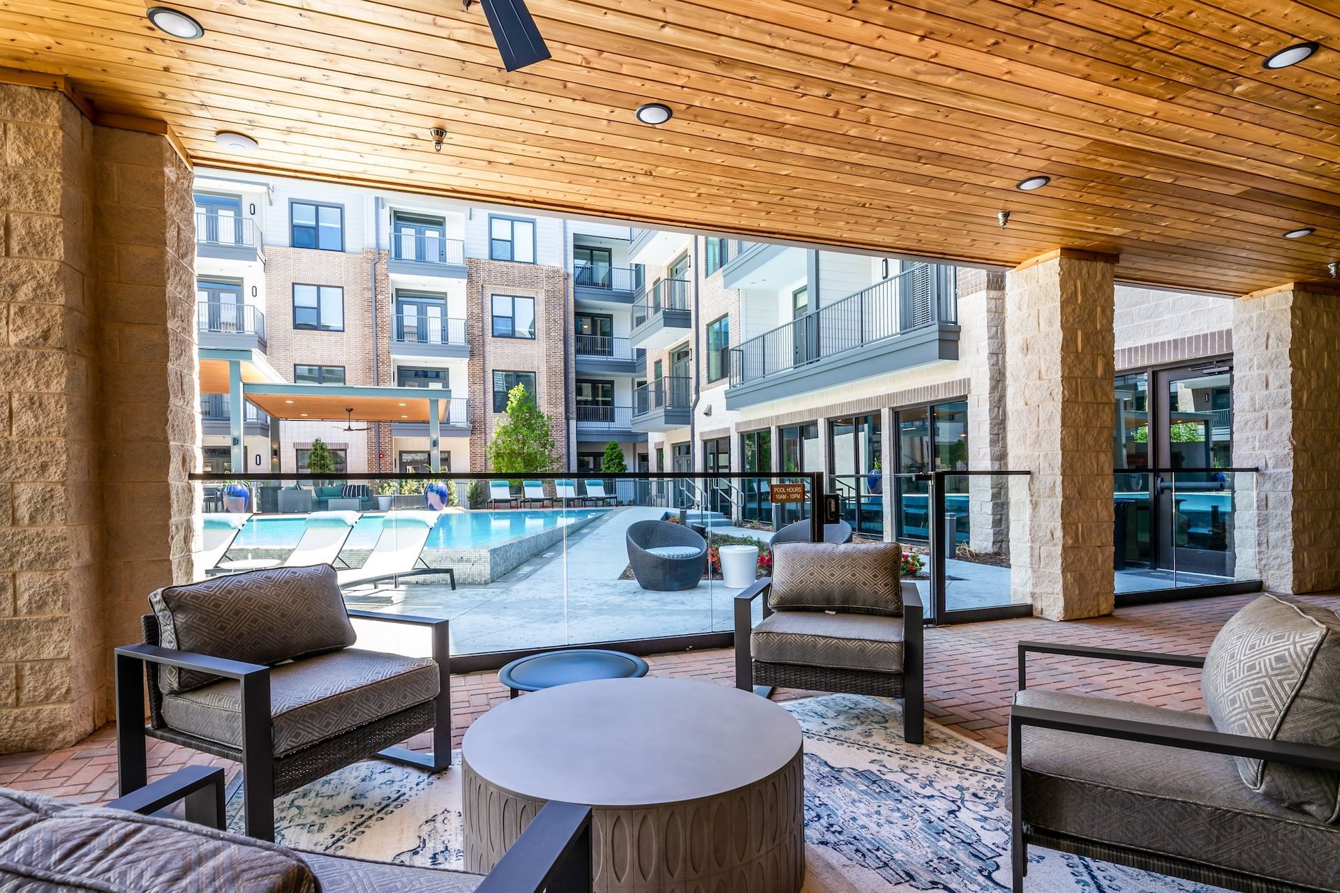 Covered outdoor patio with seating overlooking a pool and apartment buildings.