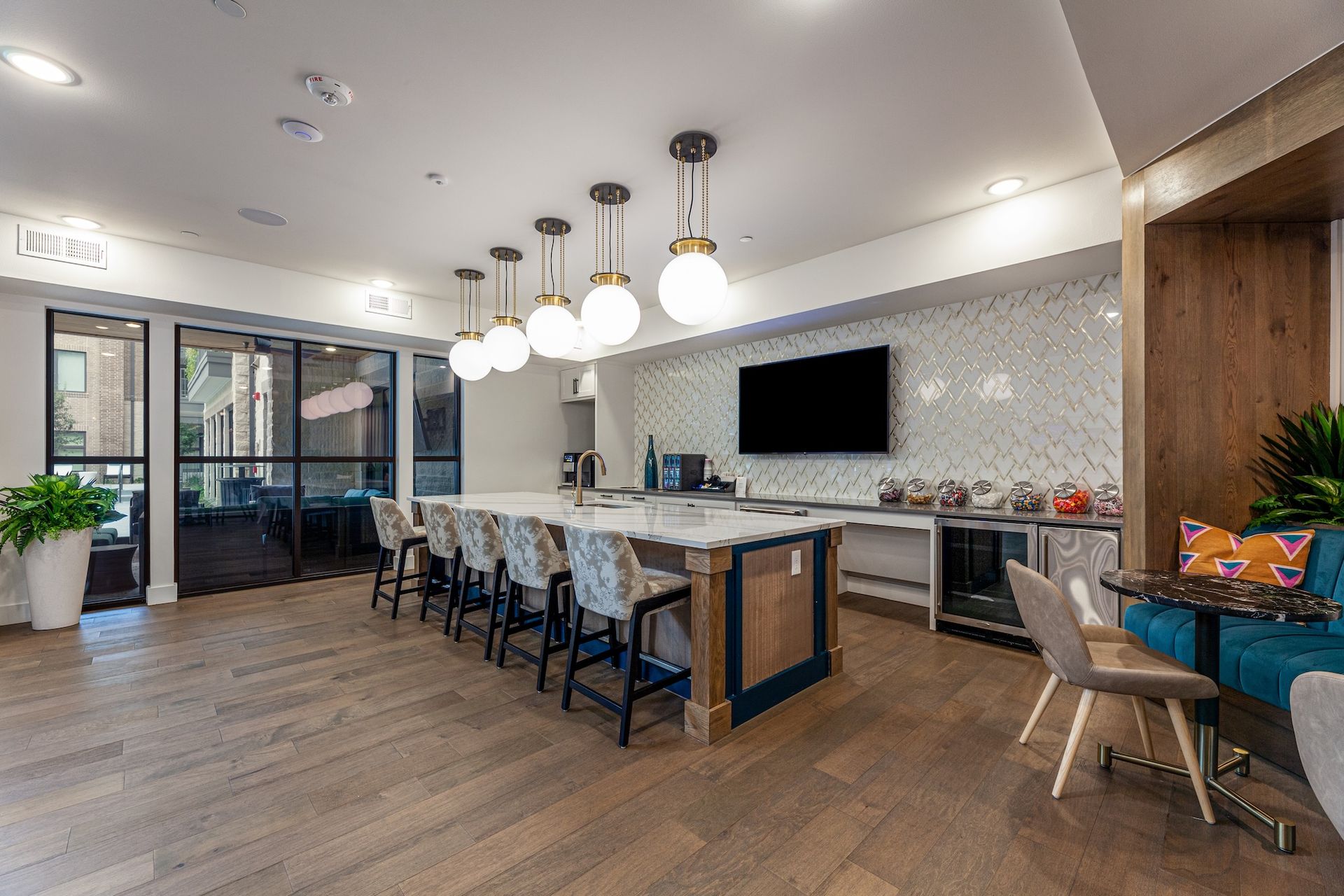 A modern apartment community kitchen area with a white marble island, bar stools, and a seating nook with blue upholstery.