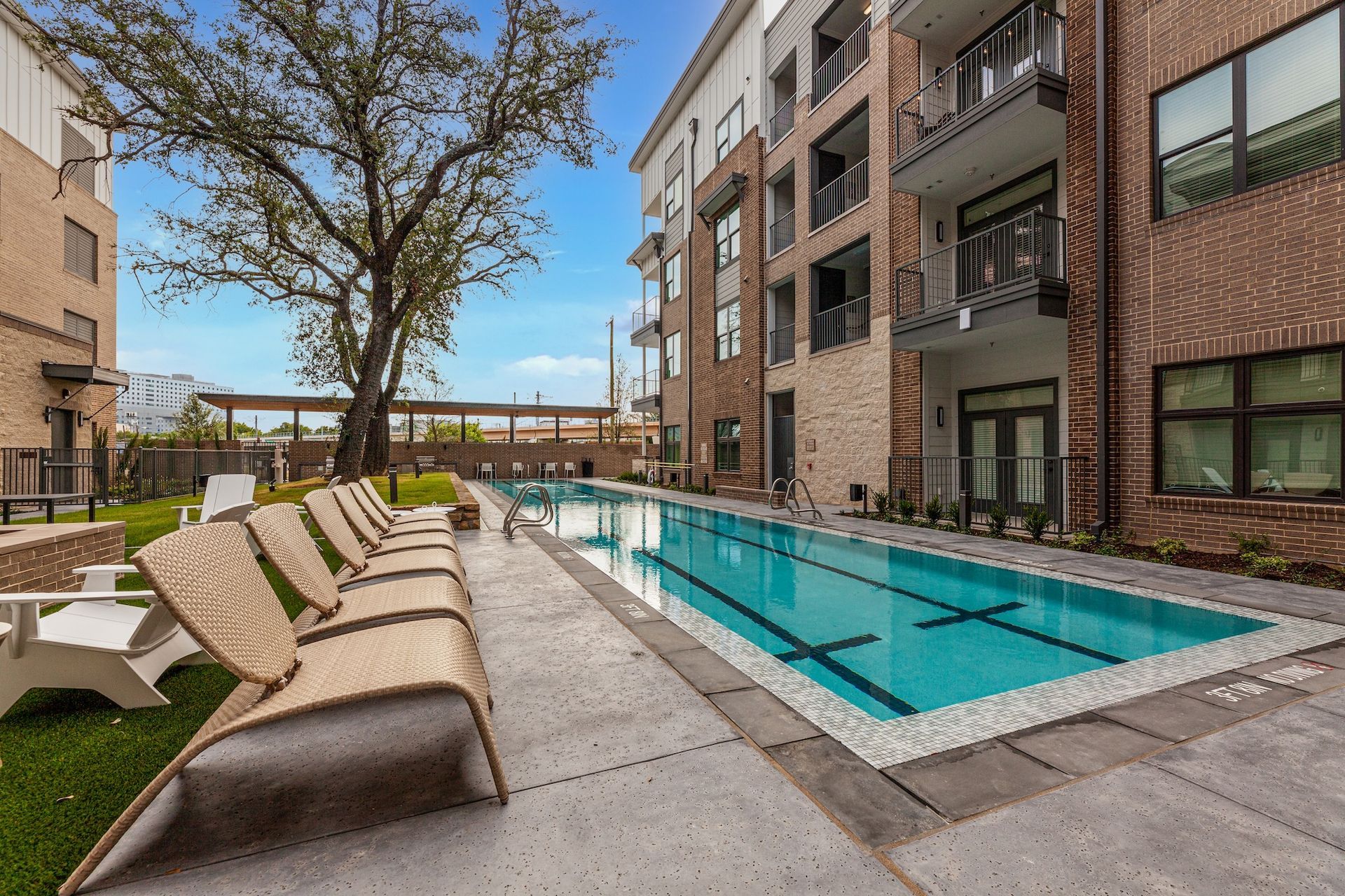 Apartment pool with lounge chairs. Buildings surround the rectangular, turquoise-tiled pool. Sunny day.