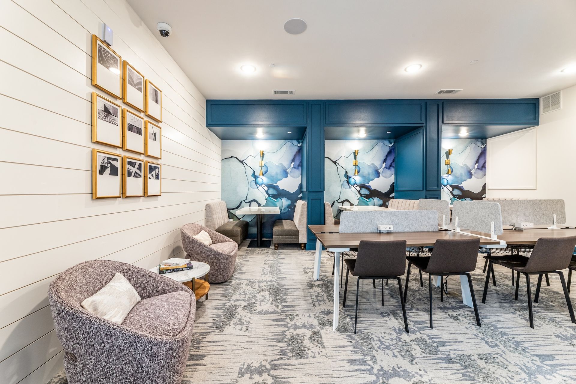 A modern co-working area with a lounge, armchairs, and tables with chairs set against a blue patterned accent wall.