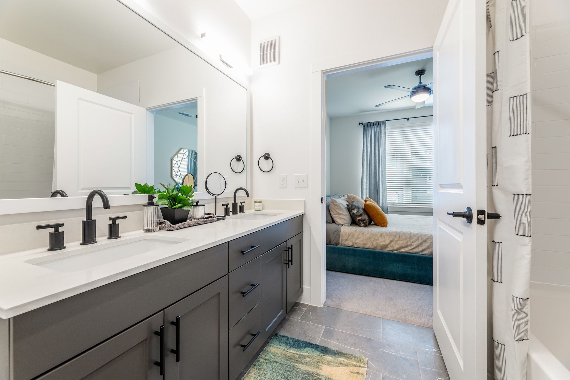 Bathroom with a double sink vanity, gray cabinets, and a doorway to a bedroom.