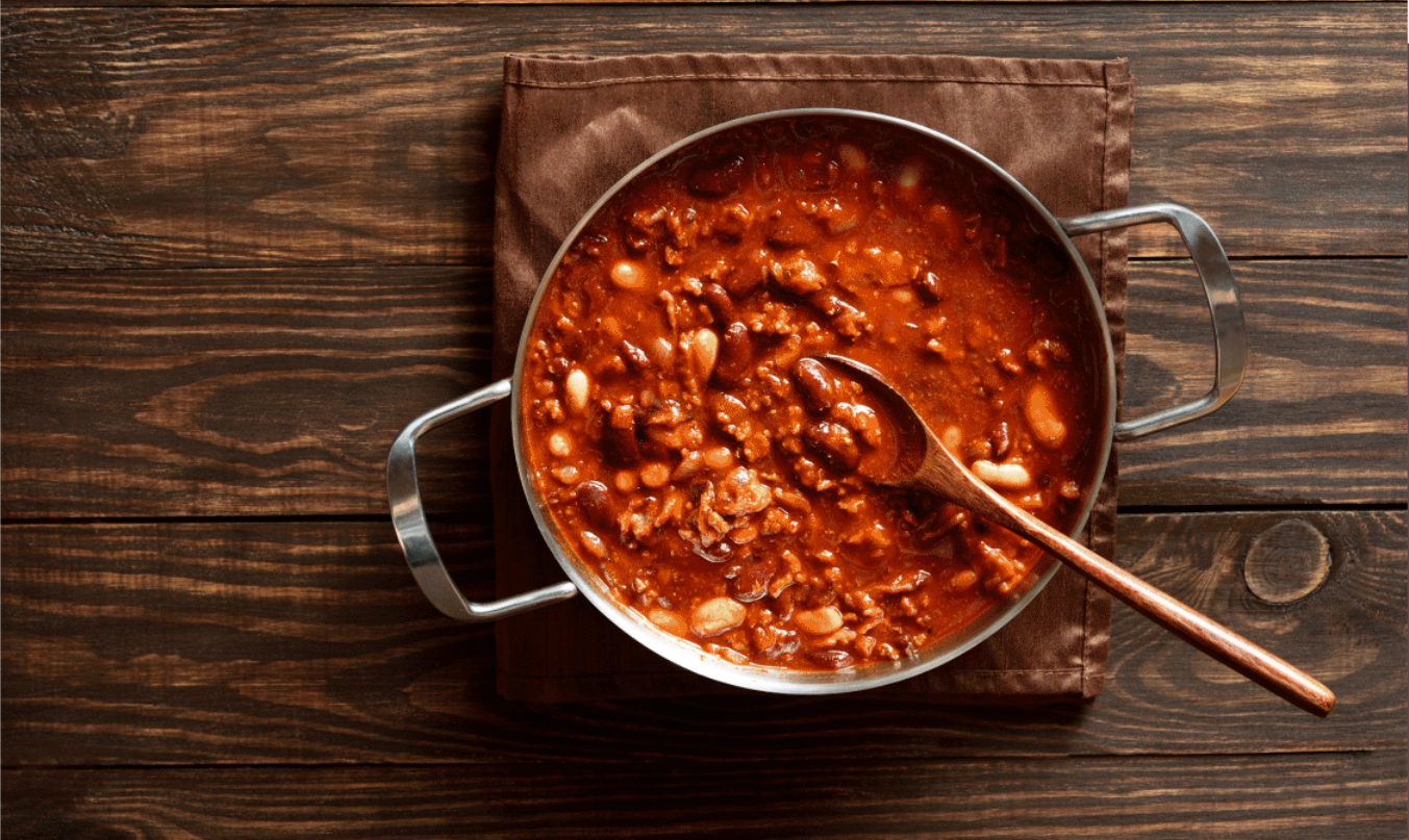 Rustic pot of red bean stew with a wooden spoon on a wooden table.