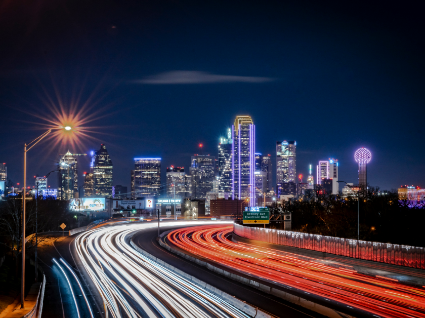 Night cityscape with traffic light trails against a dark blue sky.