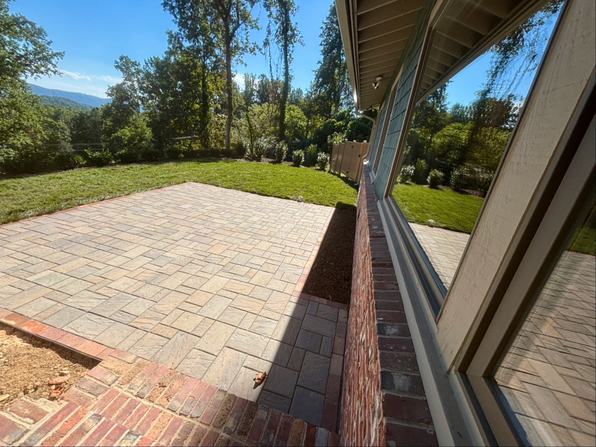 Brick patio next to a building with large windows reflecting trees and a lawn; sunny day.