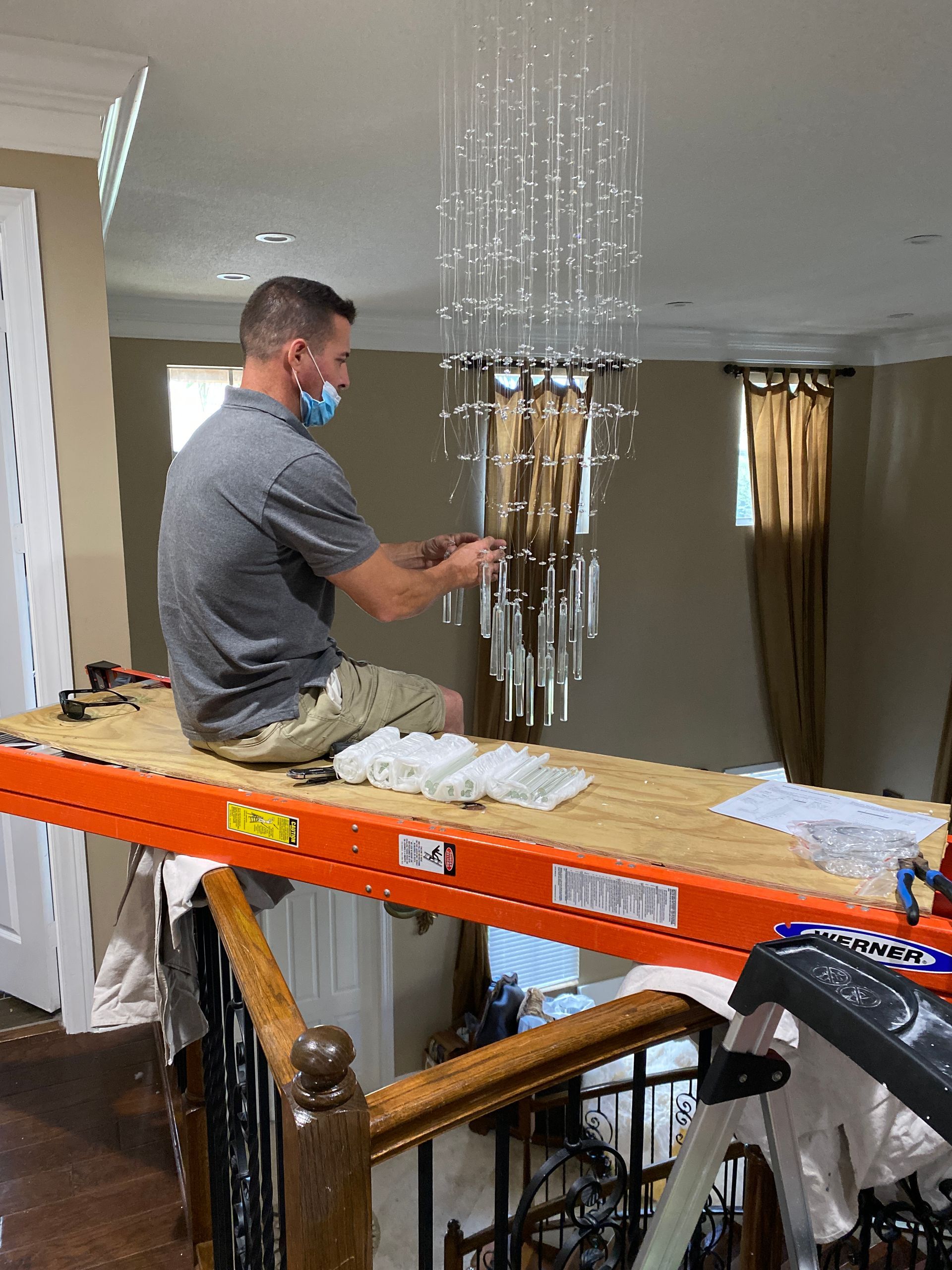 A man is sitting on a ladder working on a chandelier.