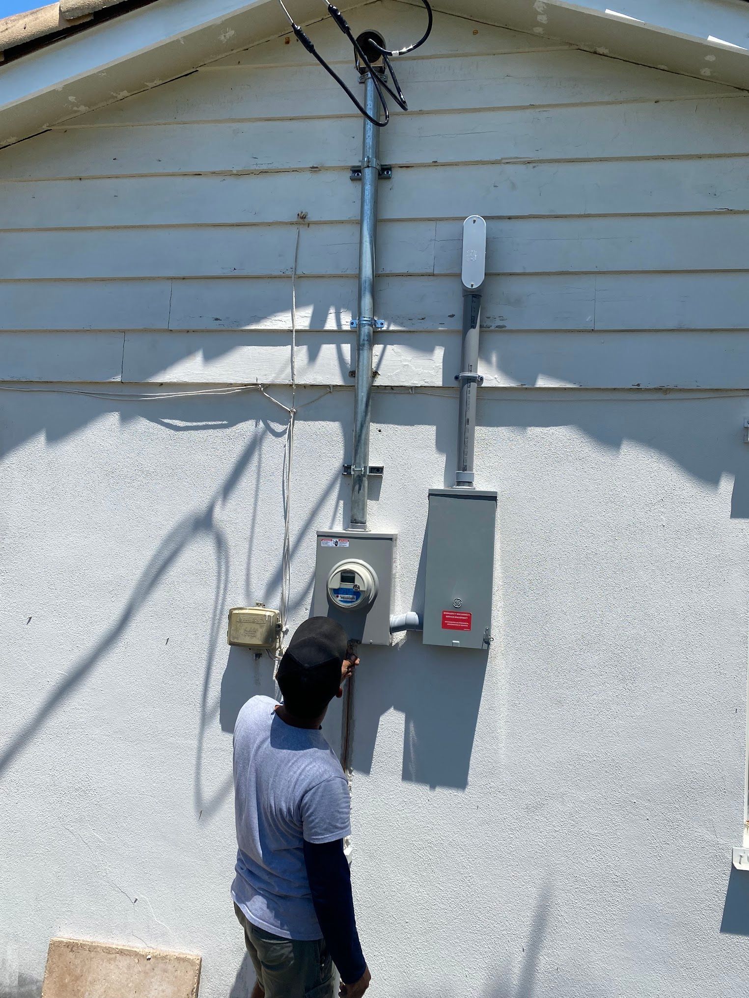A man is standing in front of a white house looking at electrical wires.