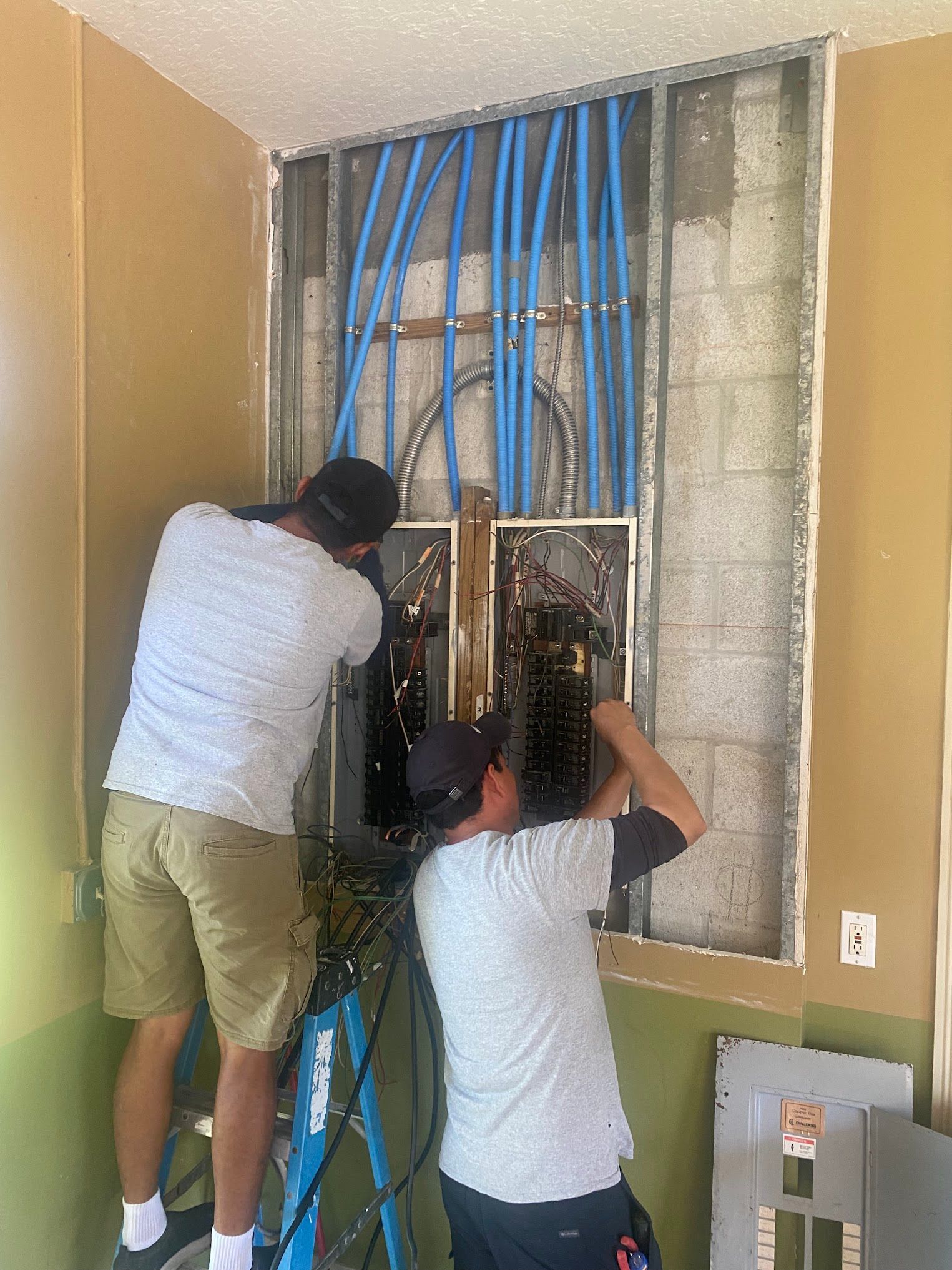 Two men are working on an electrical box in a room.