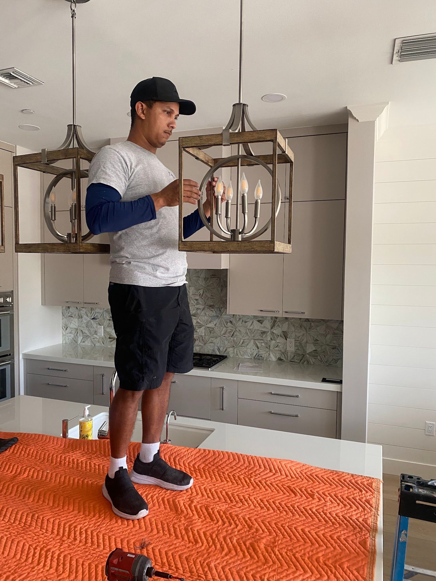 A man is installing a chandelier in a kitchen.