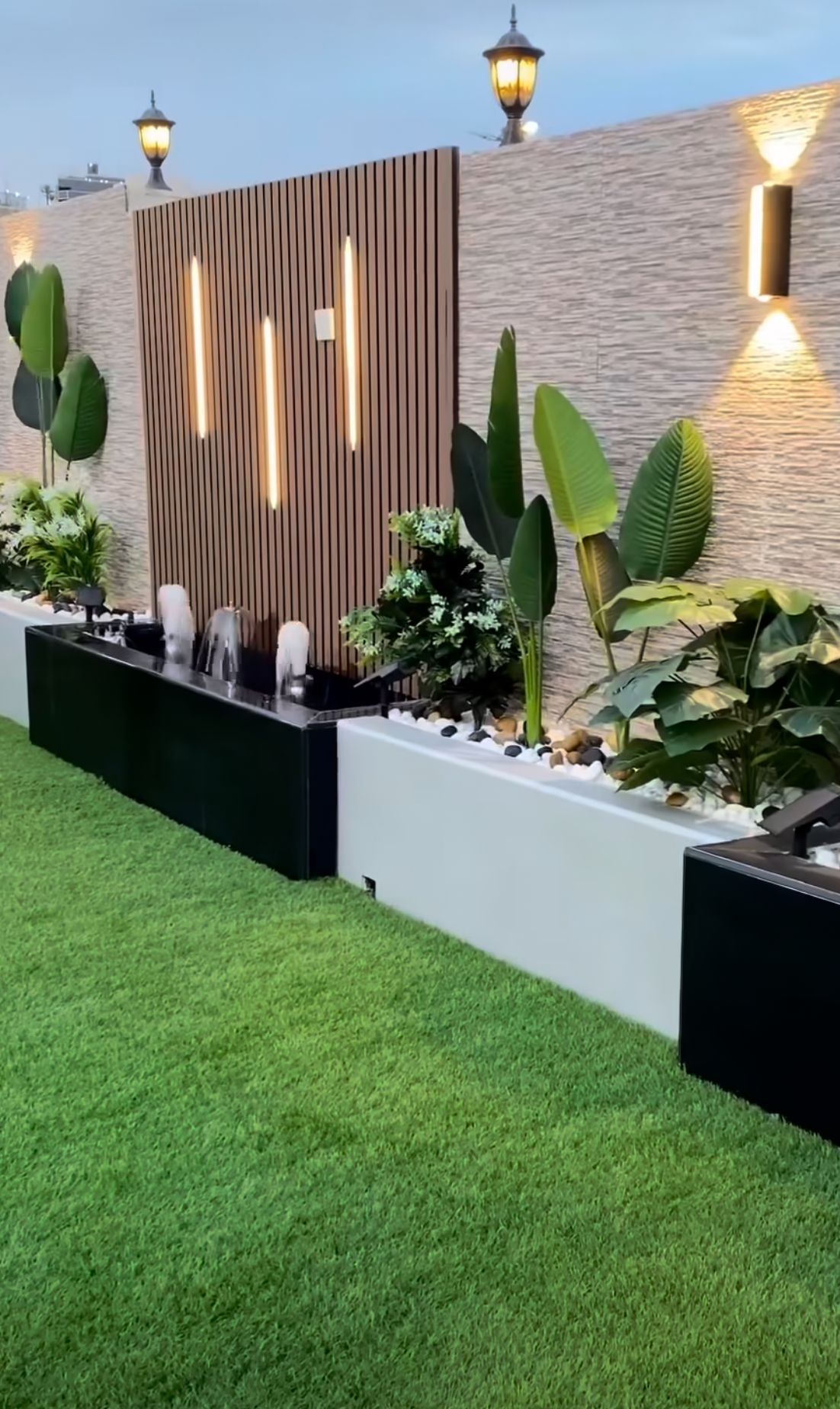 A lush green lawn with a stone wall and a fountain in the background.
