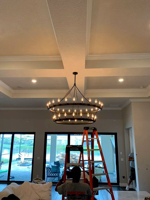 A man is sitting on a ladder in front of a large chandelier in a living room.
