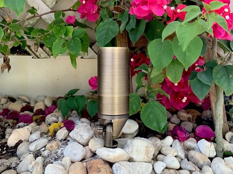 A light is sitting on a pile of rocks next to a bush with pink flowers.