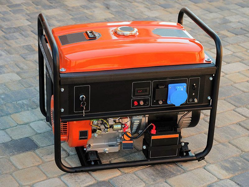 An orange portable generator is sitting on a brick sidewalk.
