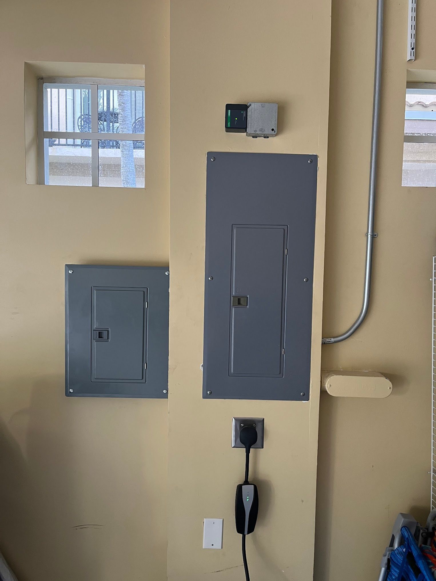 A gray electrical box is hanging on a wall next to a window.