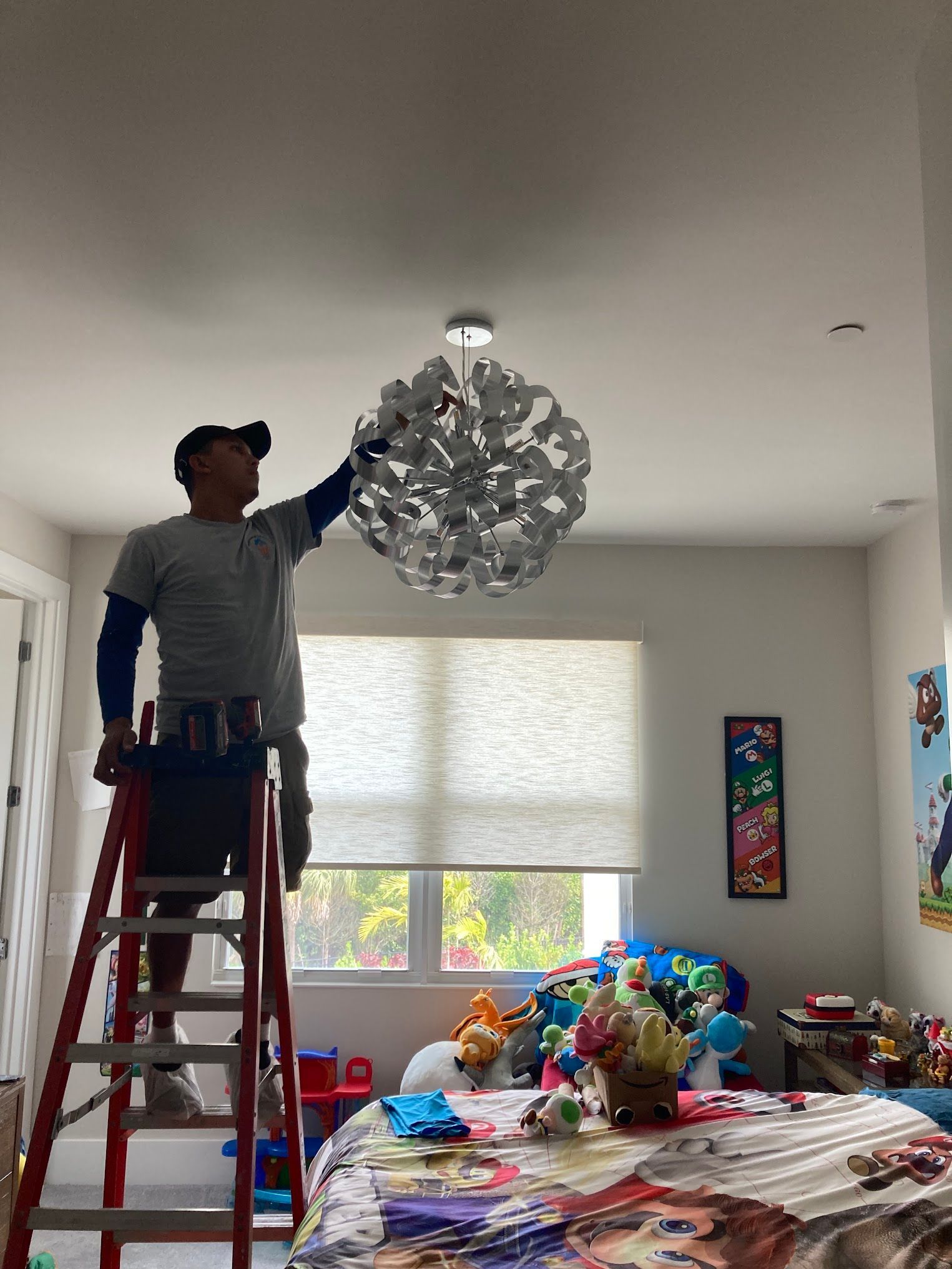 A man is standing on a ladder in a room holding a chandelier.