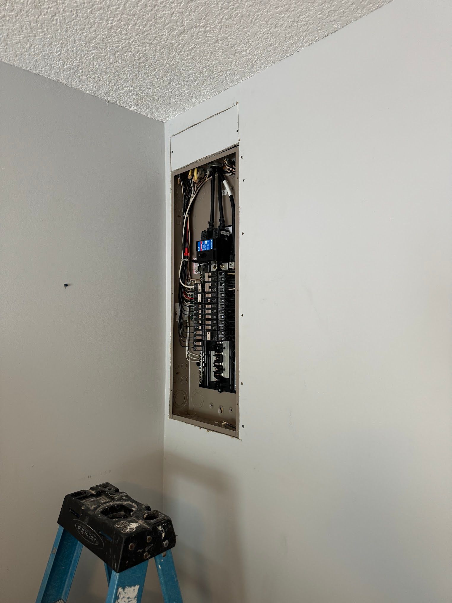 A ladder is sitting next to a wall with a electrical box in it.