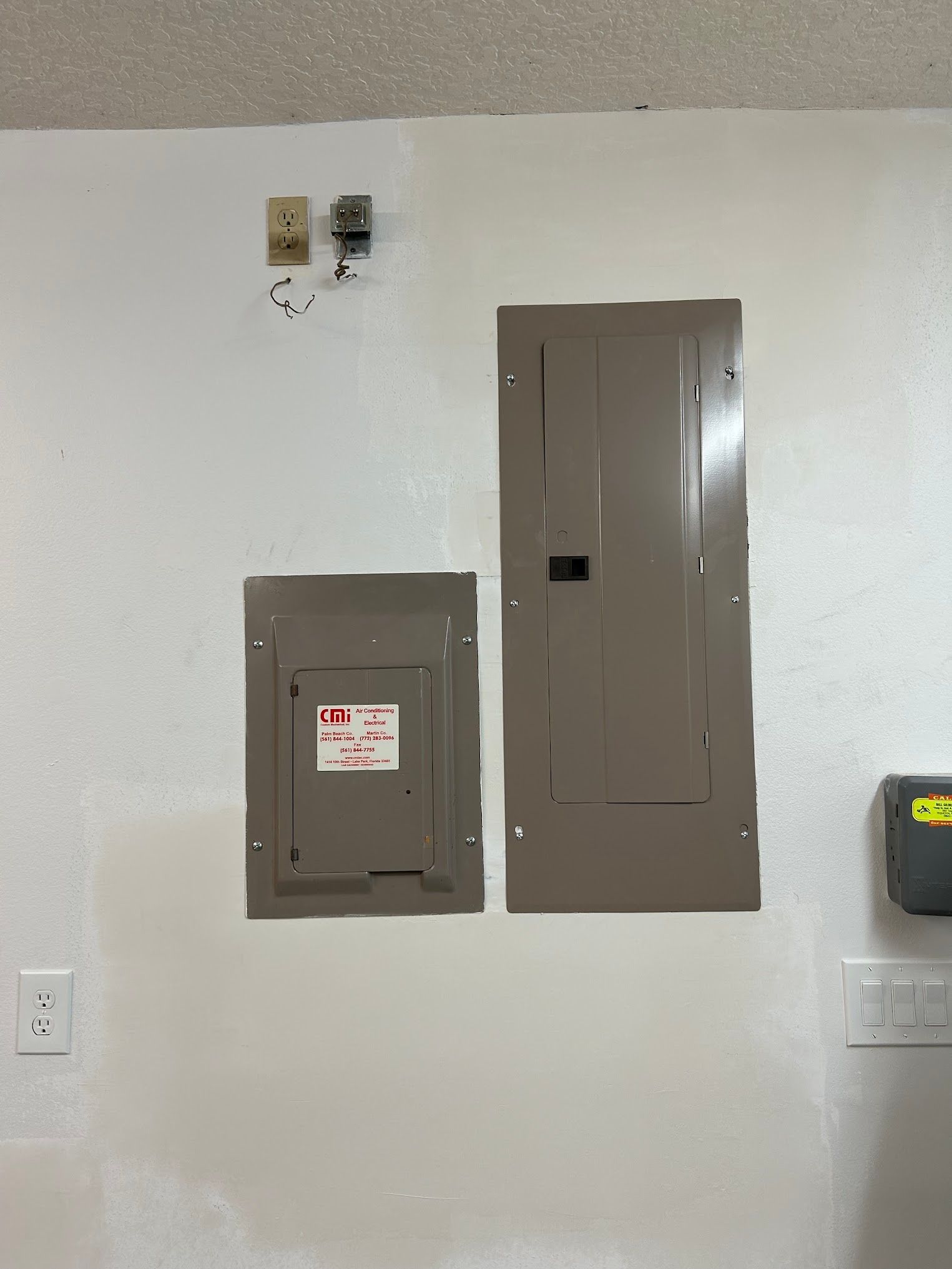 Two electrical panels are hanging on a white wall.
