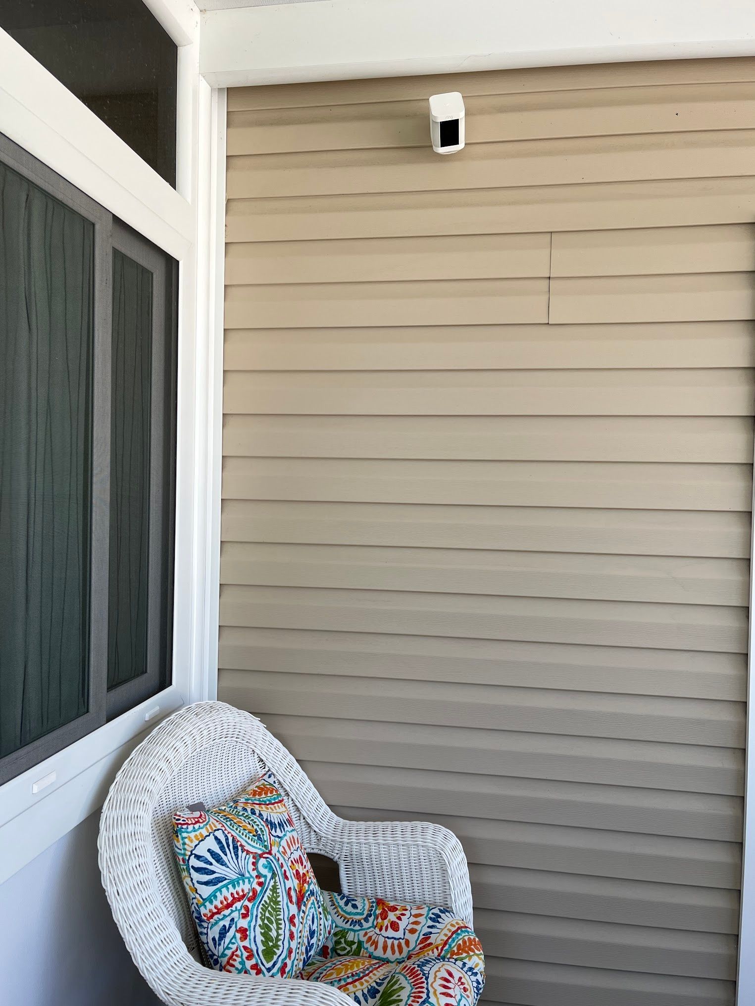 A wicker chair is sitting on a porch next to a window.
