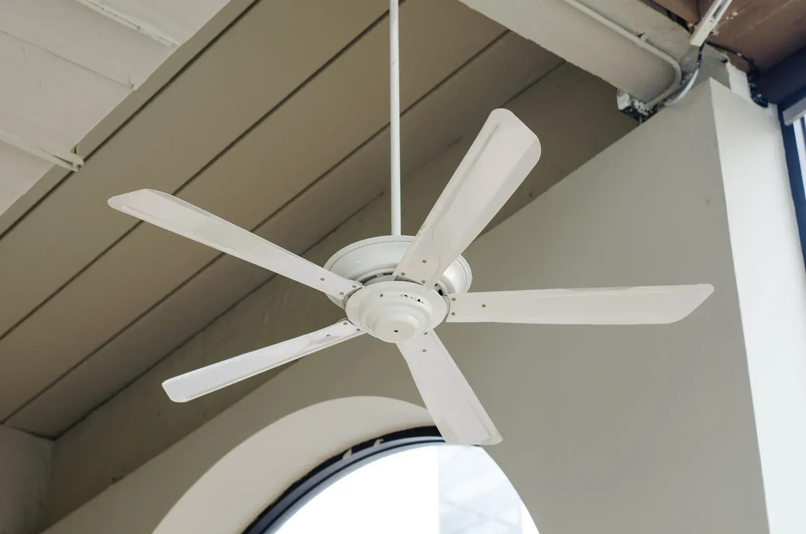 A white ceiling fan is hanging from the ceiling above a window
