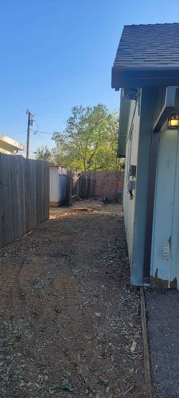 A gravel pathway between a wooden fence and a light blue building, under a blue sky.