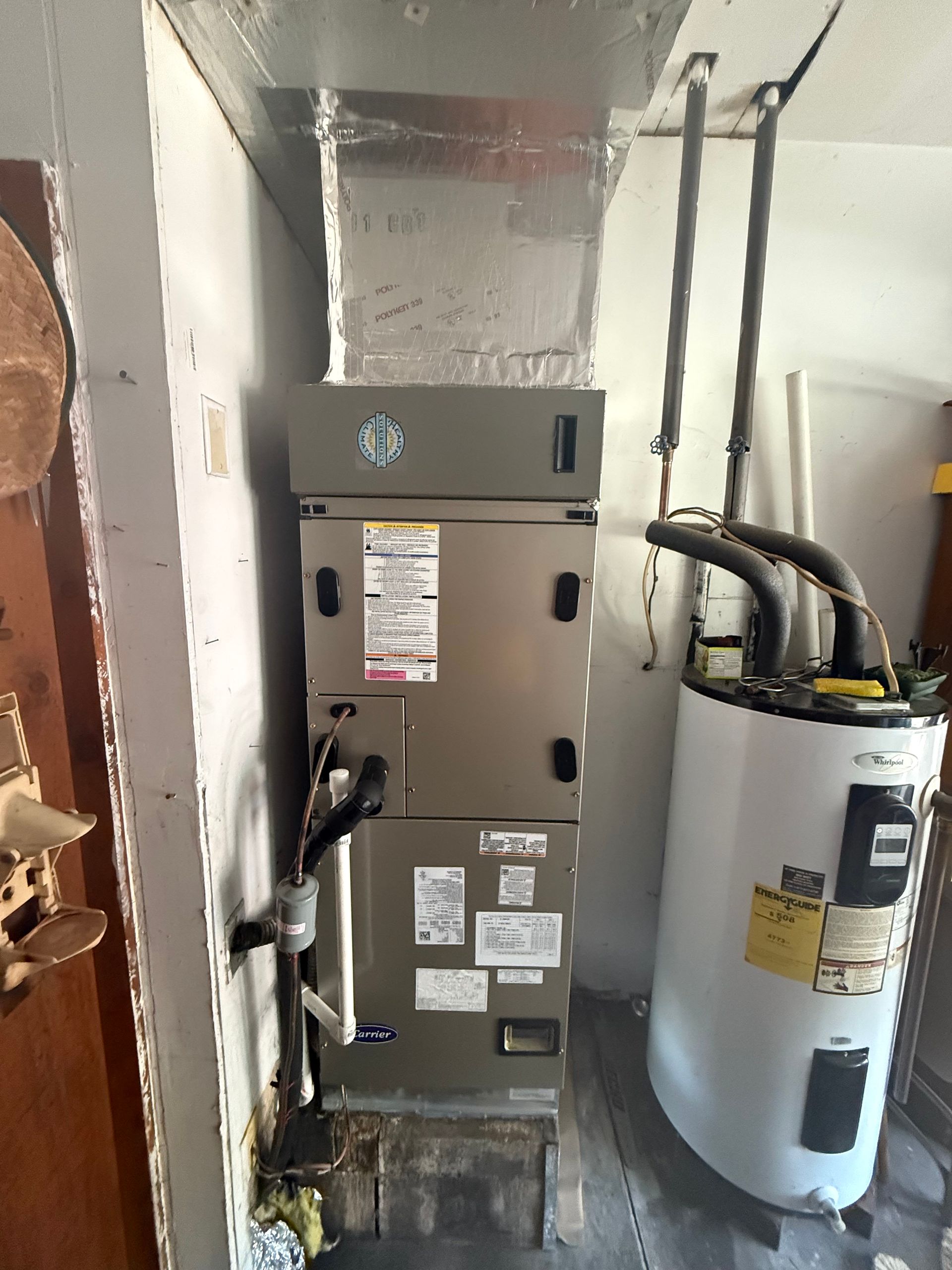 A furnace unit and a water heater stand side-by-side in a utility closet.