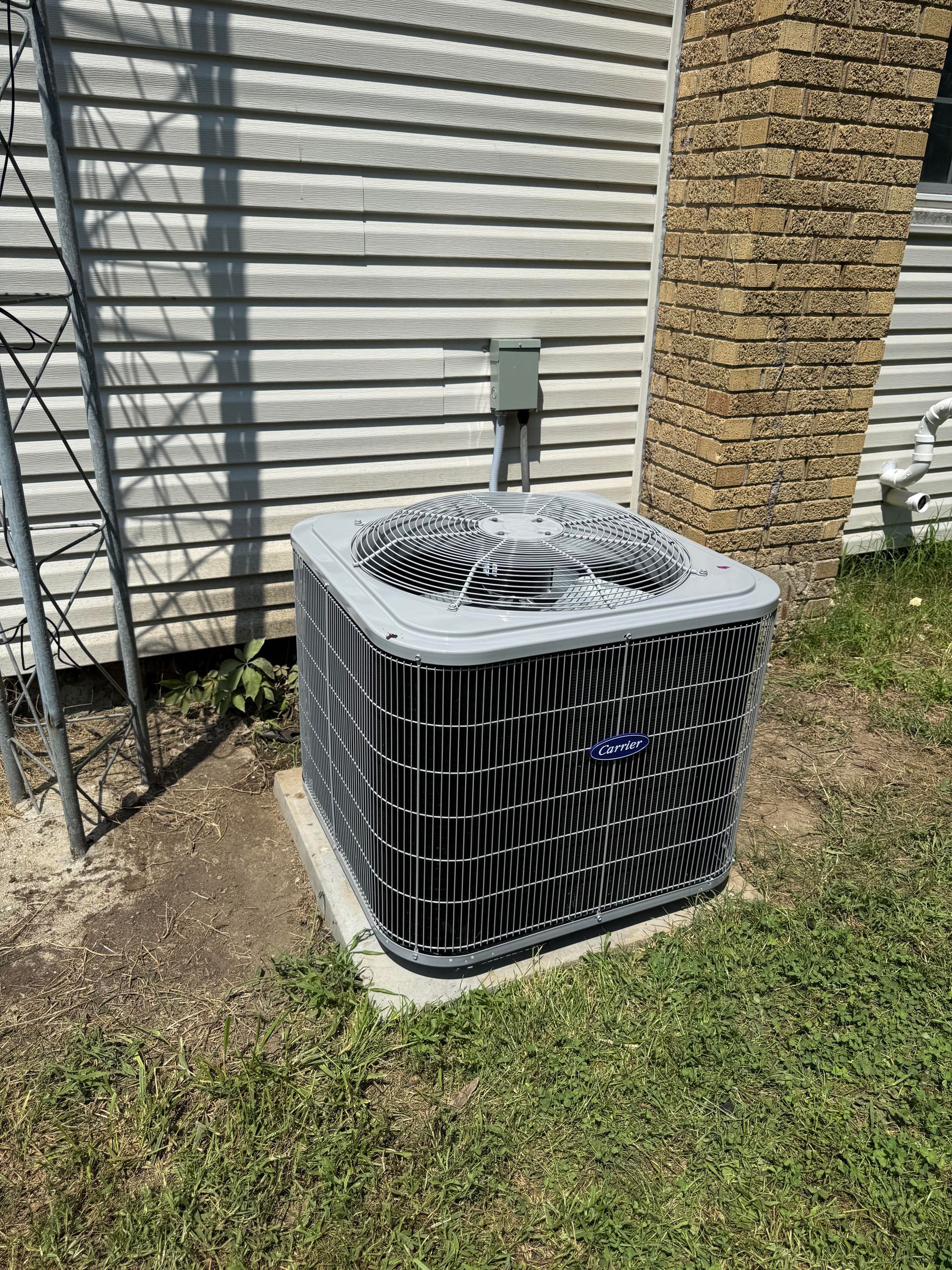A gray outdoor air conditioning condenser unit sits on a concrete pad against a house with light-colored siding.