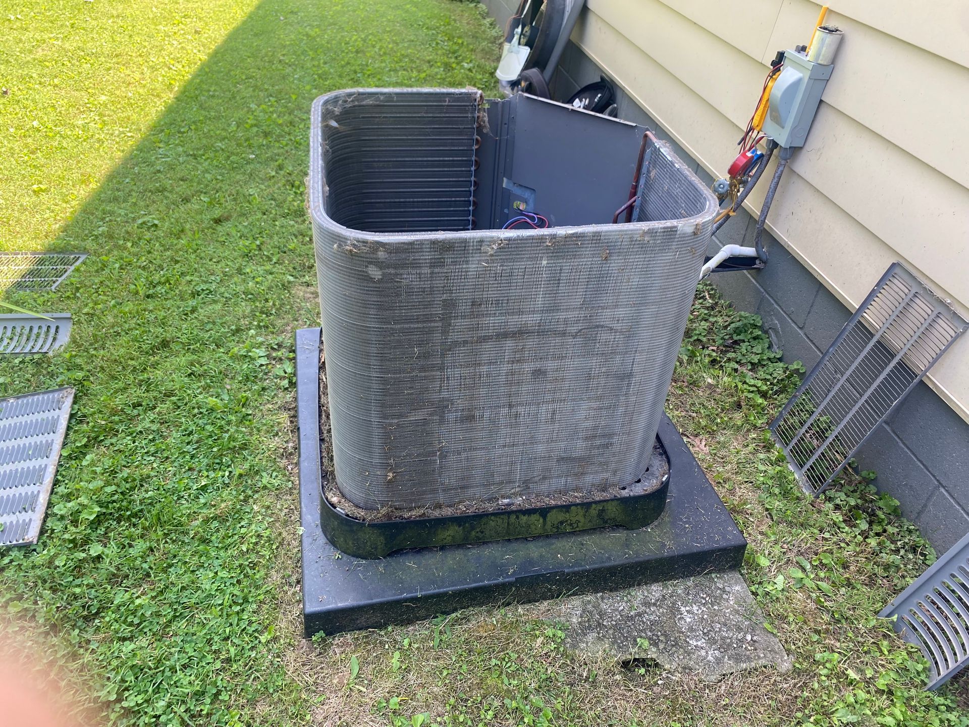 An outdoor air conditioner unit with its protective metal casing removed, sitting on a concrete pad next to a house.